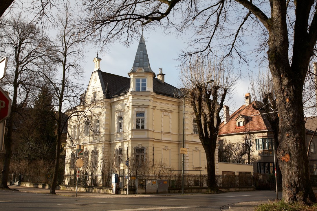 Cream-colored mansion with pointed turret and dark roof surrounded by bare trees in Saggen, Innsbruck.