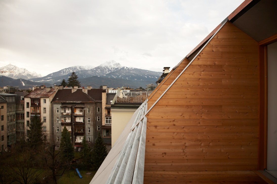 Wooden terrace railing with snowy Alpine mountain peak and Innsbruck buildings in background.