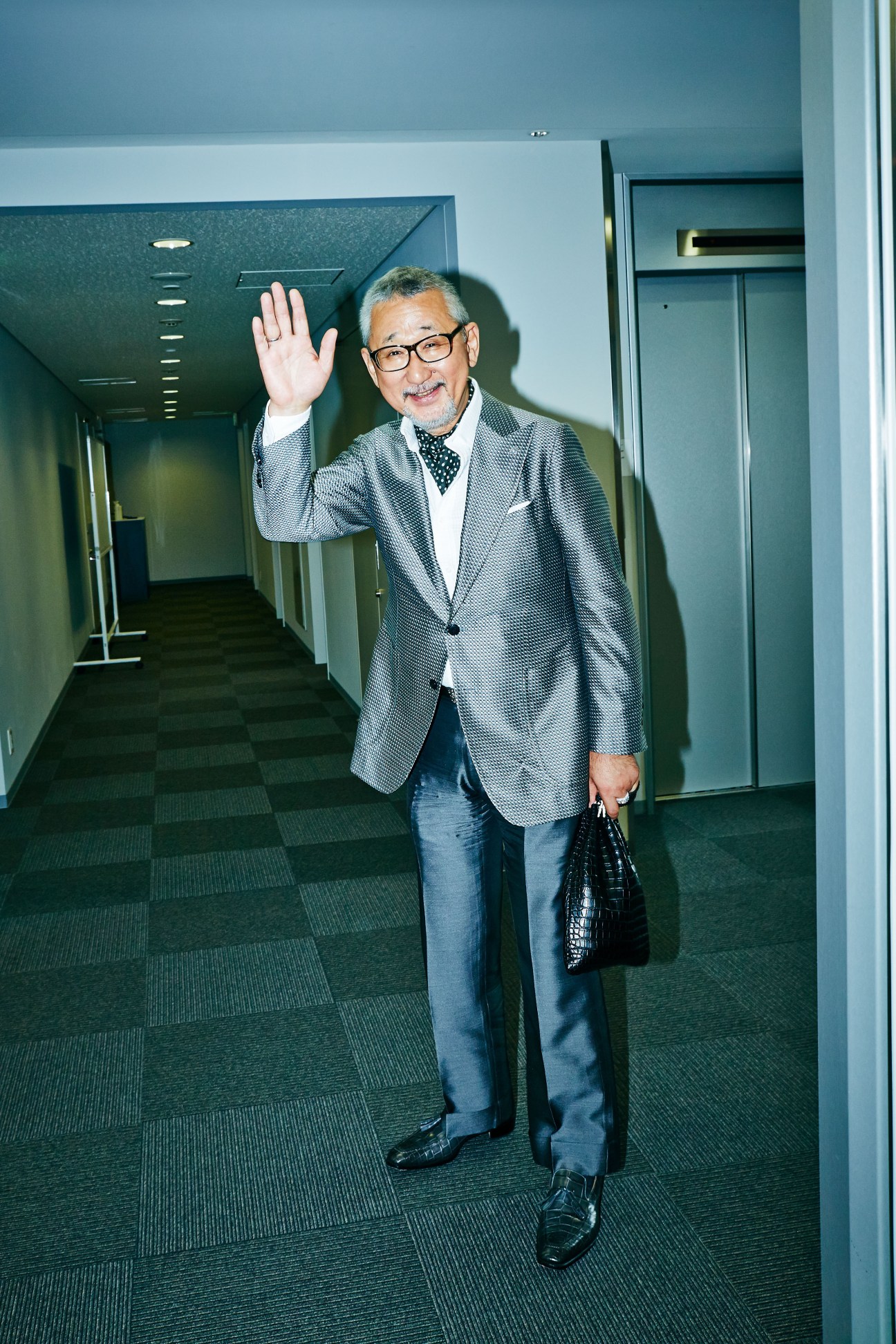 Osamu Shigematsu, United Arrows' honorary chairman, waving in an office corridor while holding a crocodile-skin bag.