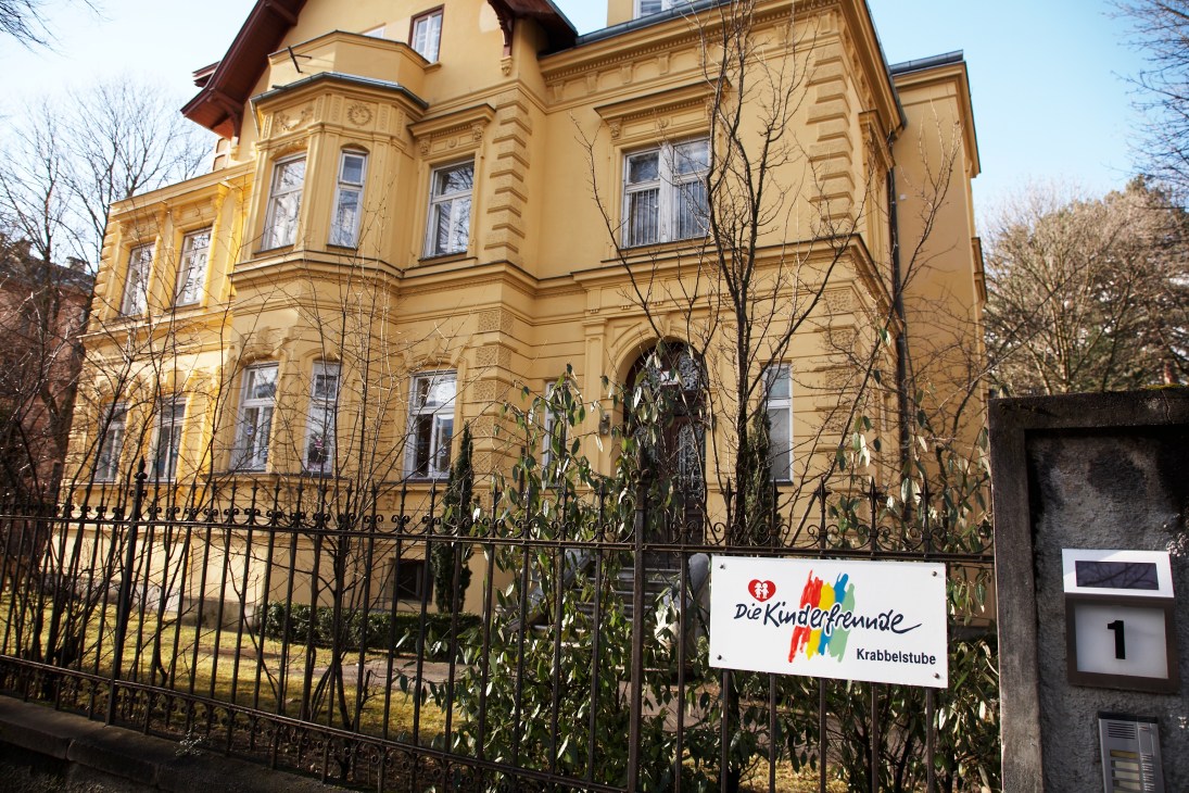 Yellow mansion with black iron fence and Kinderfreunde Krabbelstube kindergarten sign in Innsbruck.