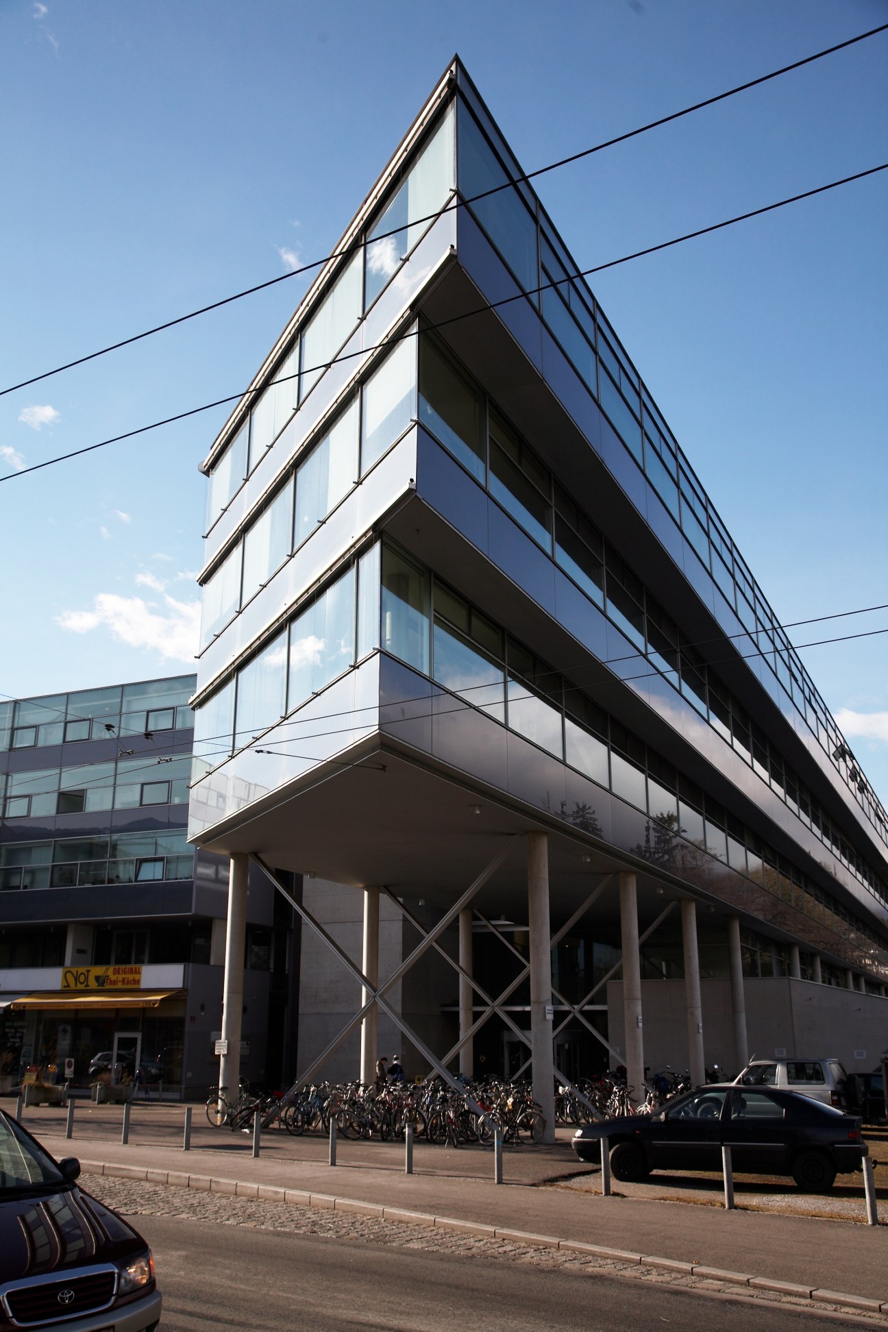 Modern glass and steel university building with angular architecture and ground-level open colonnade.