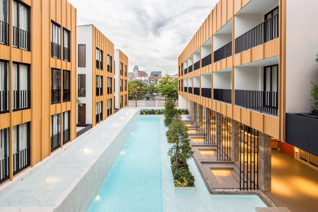 The Craftsman hotel courtyard in Bangkok with wooden-clad buildings, turquoise pool and black railings.