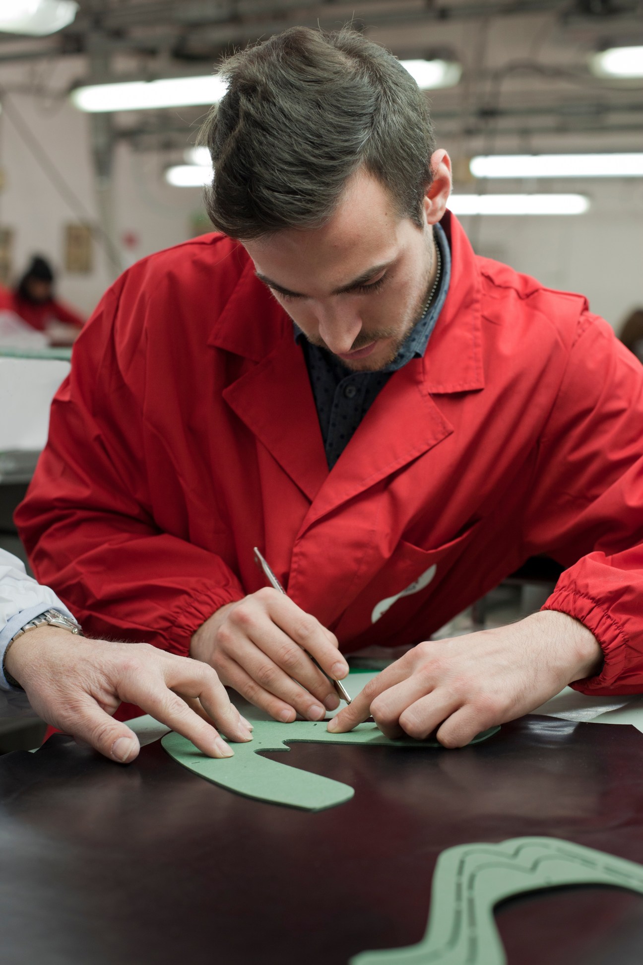 Young shoemaker Matteo Valle cuts green calf leather at a workbench in a Santoni factory workshop.