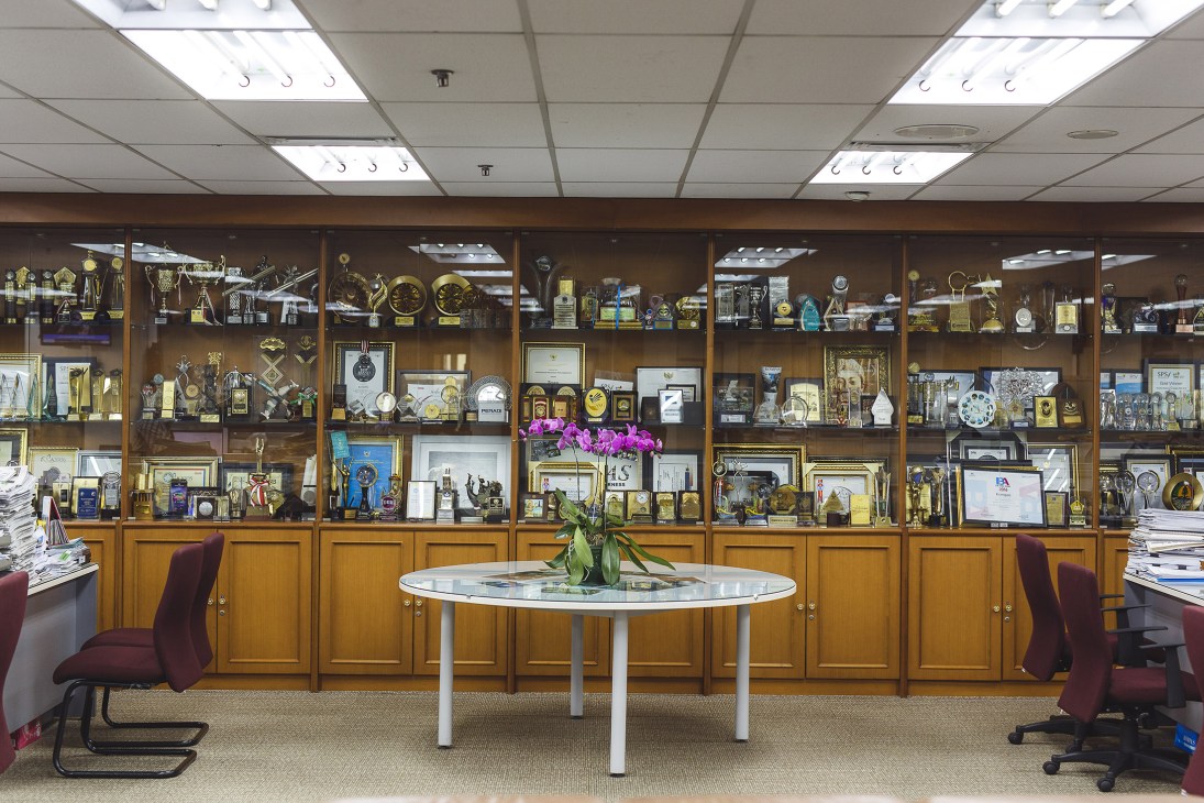 Kompas newsroom awards display with trophies and accolades behind glass cabinets and a round table with flowers.