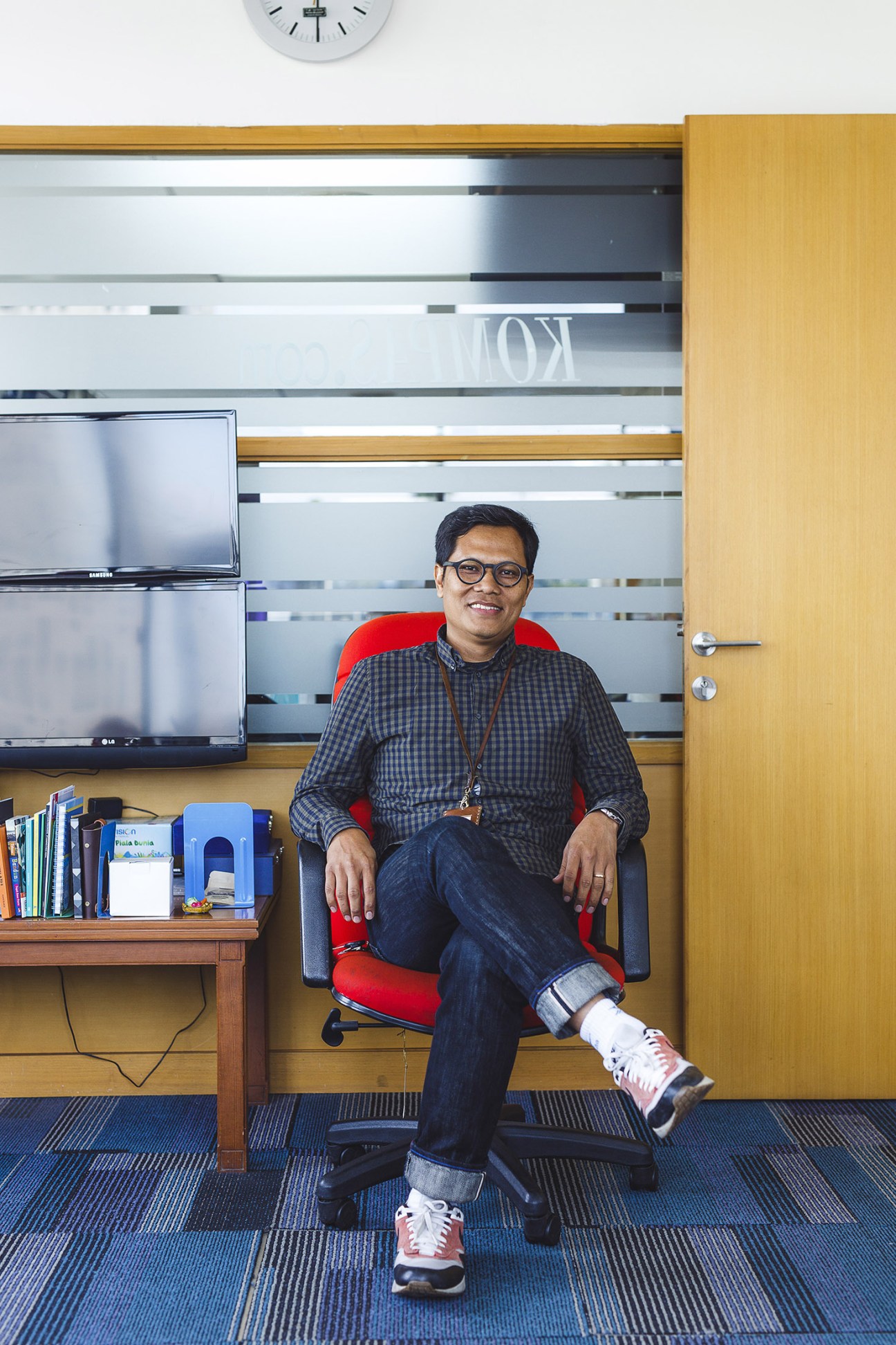 Wisnu Nugroho, editor in chief of kompas.com, sits in a red chair in his office.