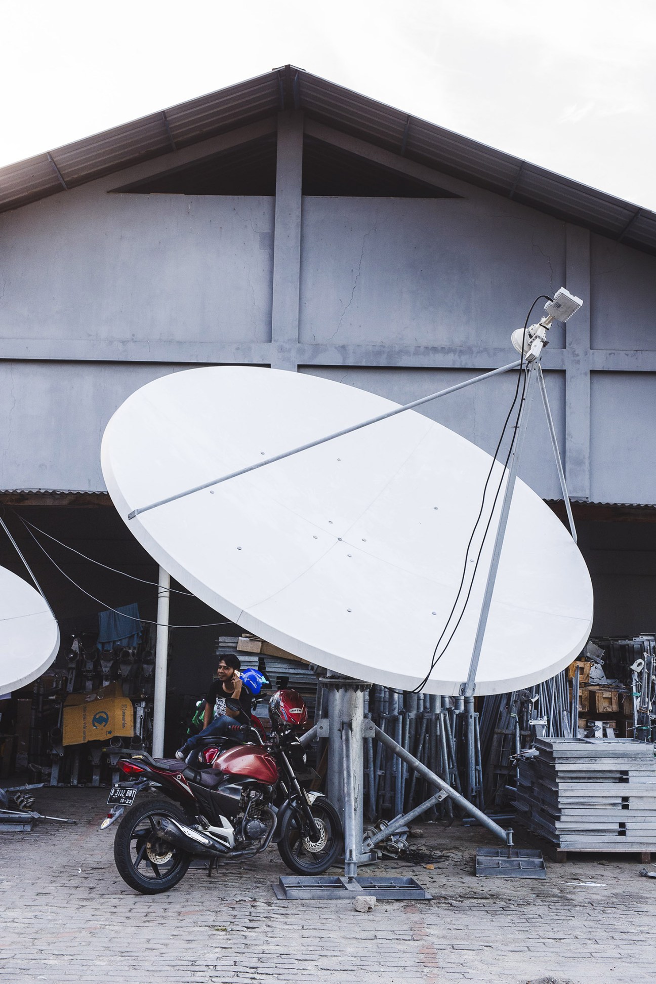 A satellite dish mounted on a concrete structure with a motorcycle parked underneath in a storage facility.