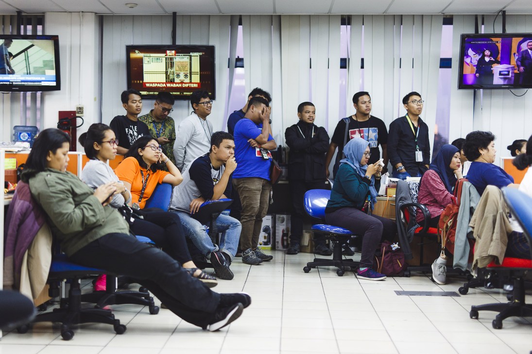 Kompas.com staff gathered in a modern office space with blue chairs during a daily department meeting.