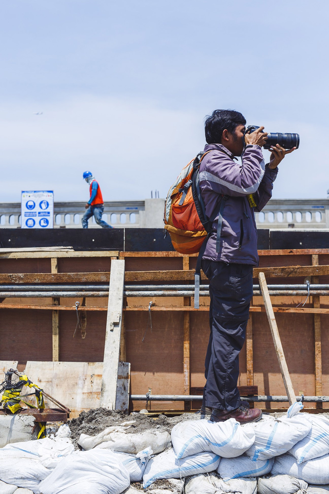 A photographer at Kompas newspaper stands on a rooftop holding a camera, capturing images during an assignment.