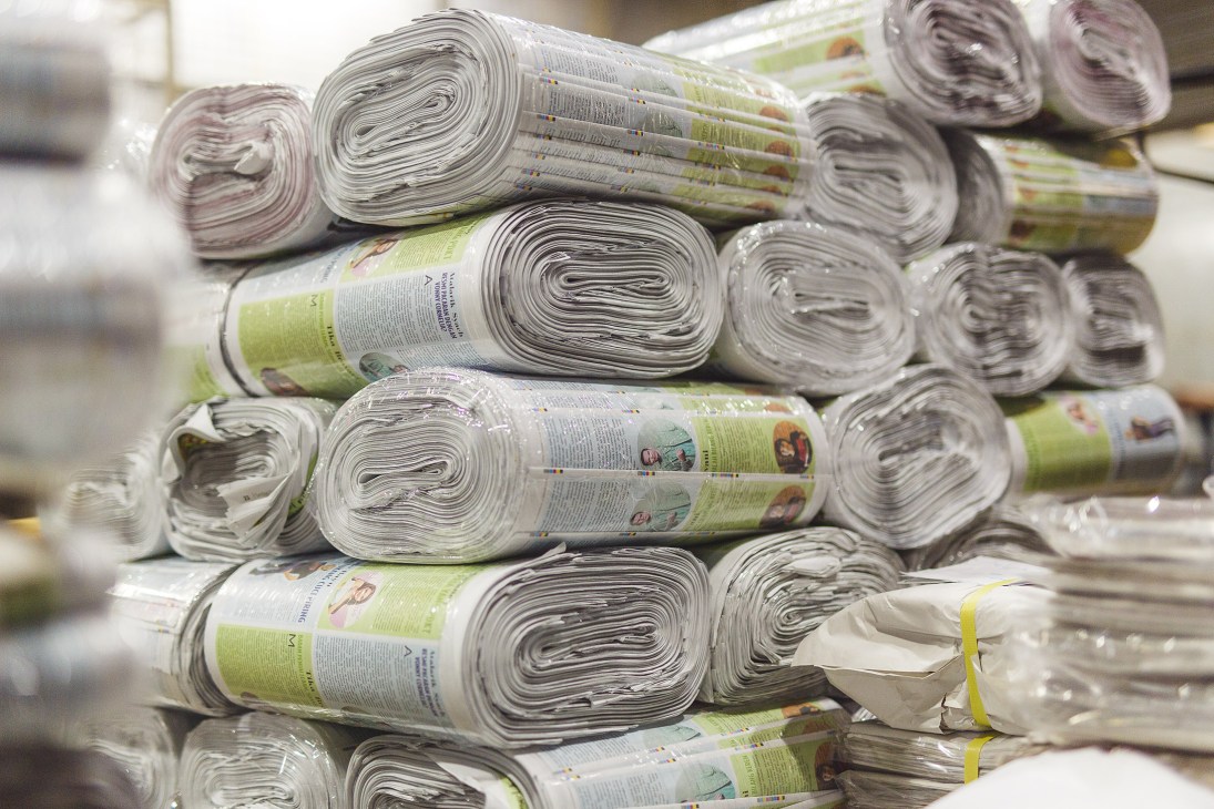 Stacked bundles of Kompas newspapers wrapped with green bands ready for distribution.