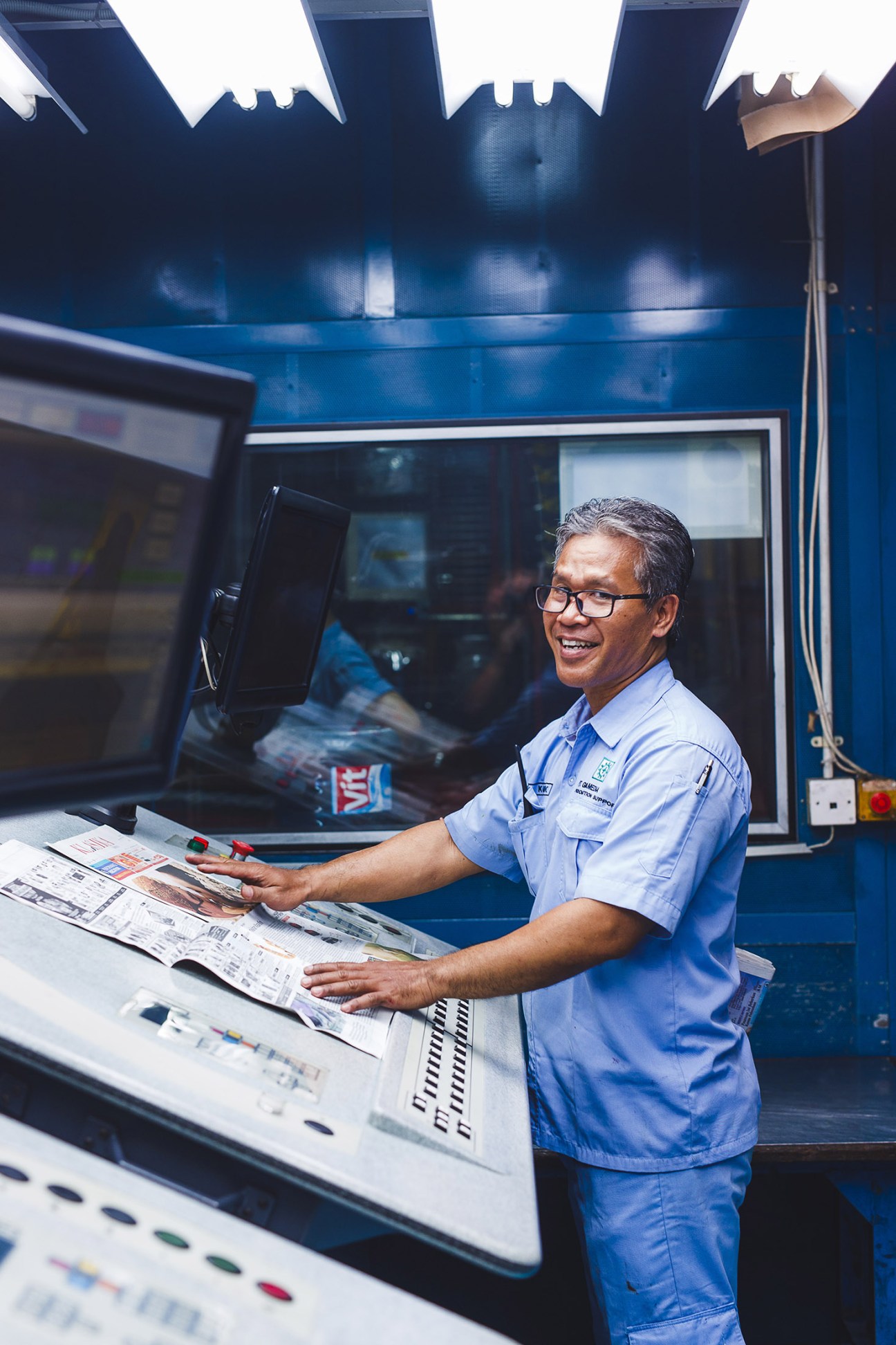 Worker in blue uniform inspecting freshly printed Kompas newspapers at the printing house.