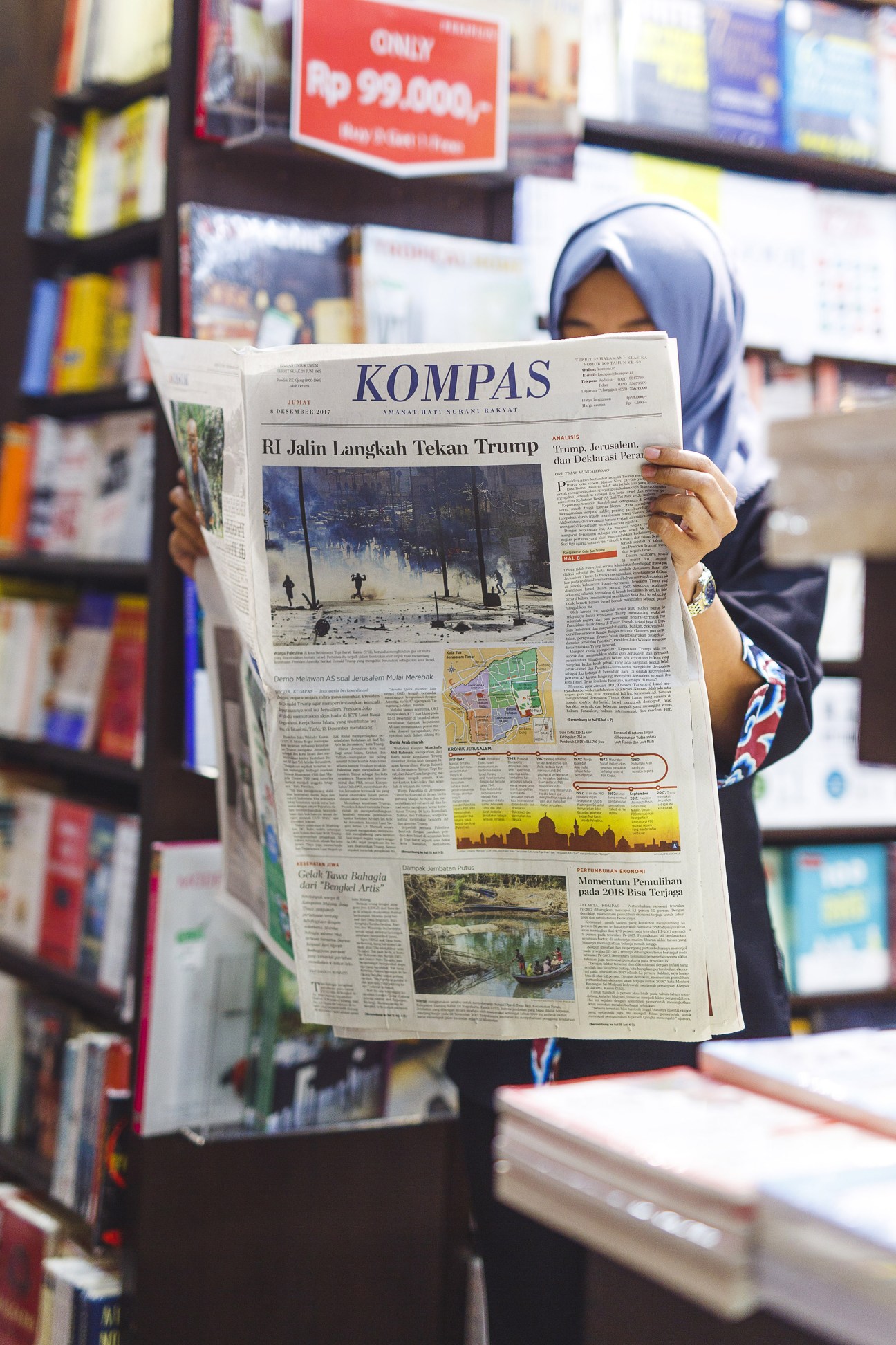 Woman wearing a blue hijab reading the Kompas newspaper in an airport bookshop.