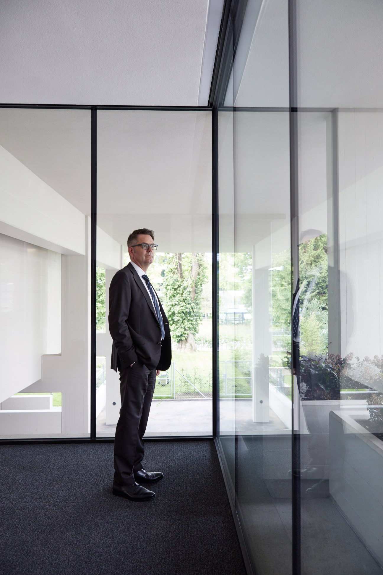 Michael Müller, CEO of Ledermann Immobilien, stands in a modern white interior with floor-to-ceiling windows overlooking a park.