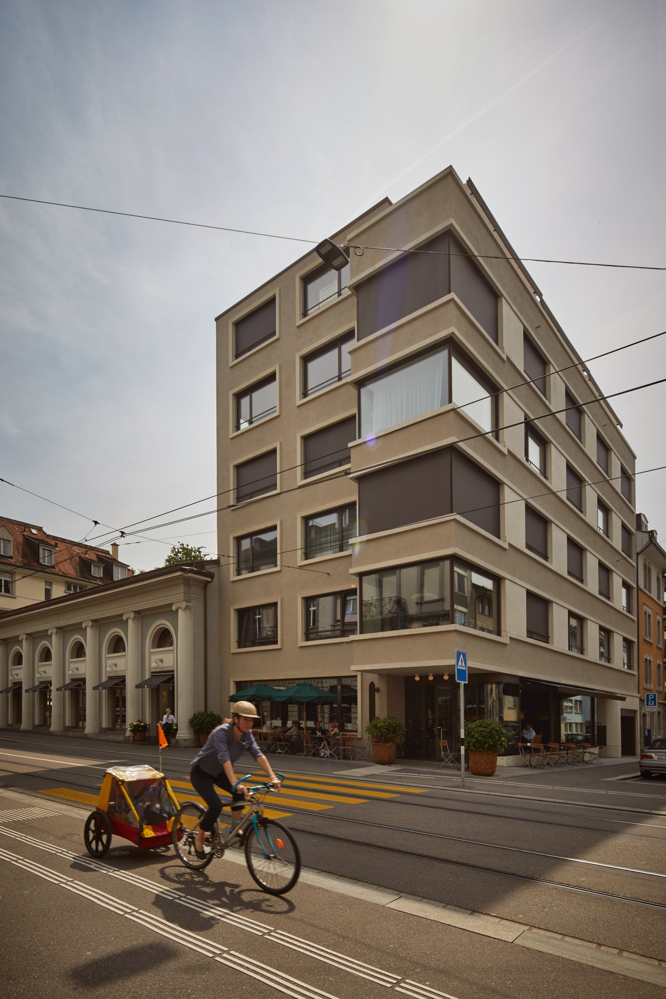 Tan-colored residential building with regular window pattern on a Zürich street with cyclist and tram tracks
