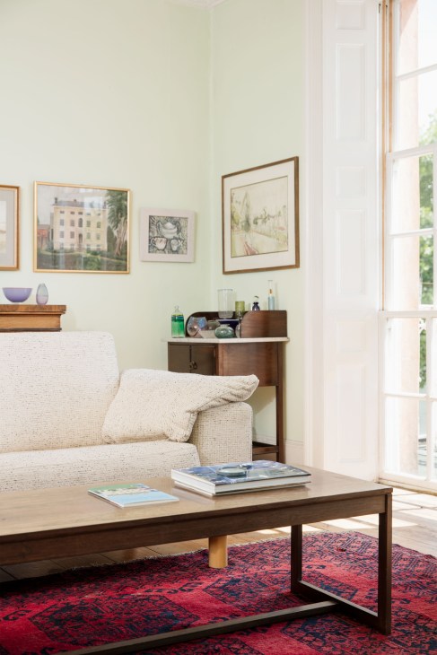 Light-filled sitting room with cream bouclé sofa, mid-century wooden coffee table, framed artworks, and displayed glassware.