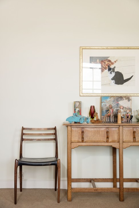 Mid-century wooden chair beside wooden desk displaying folk art paintings and decorative objects including a blue toy car.