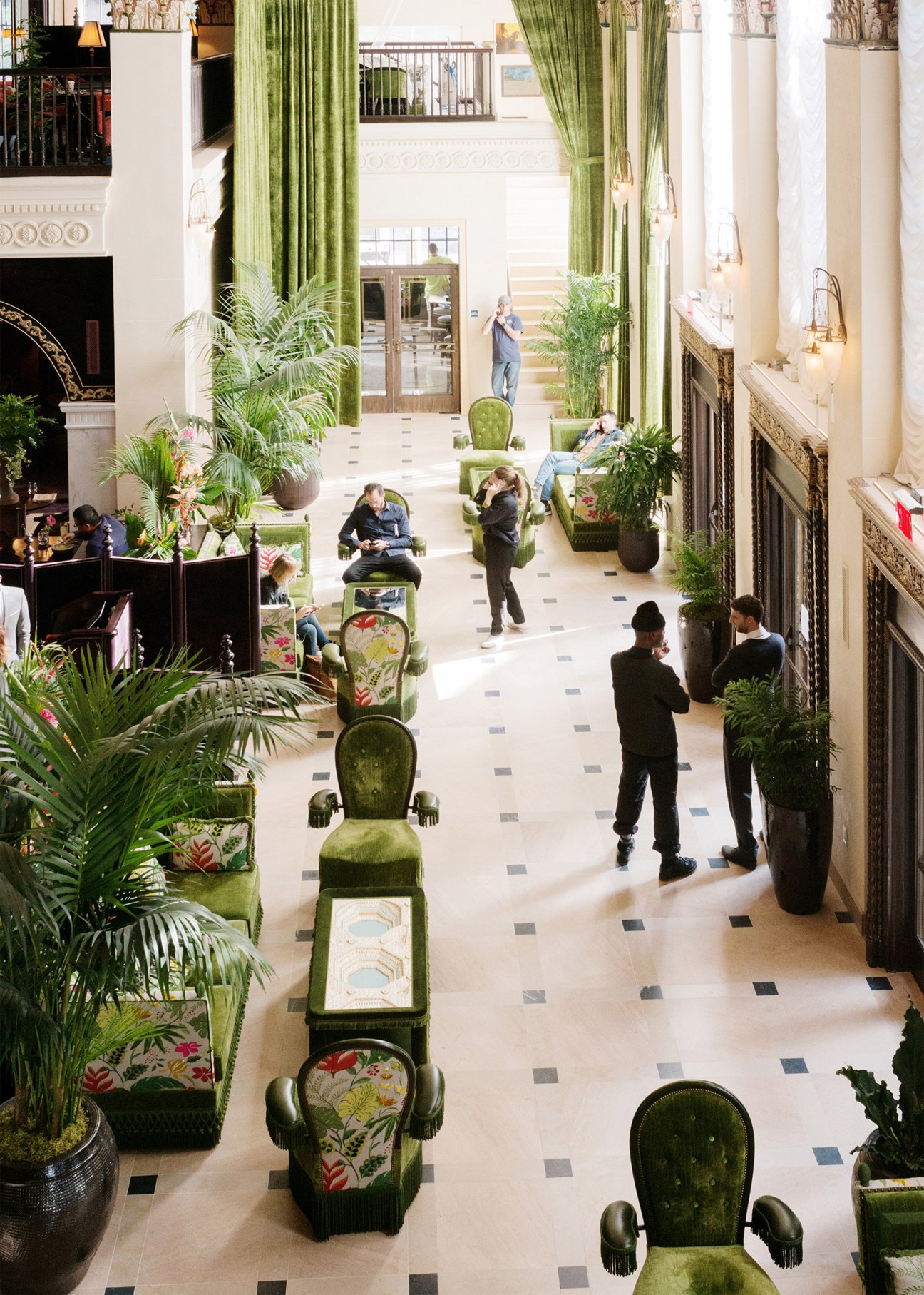 Overhead view of NoMad Los Angeles lobby with green velvet chairs, potted plants, and guests walking on marble floors.