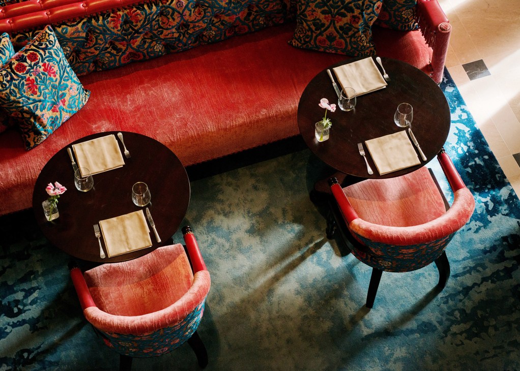 Overhead view of red velvet seating with ornate patterned cushions and round black tables set for dining.