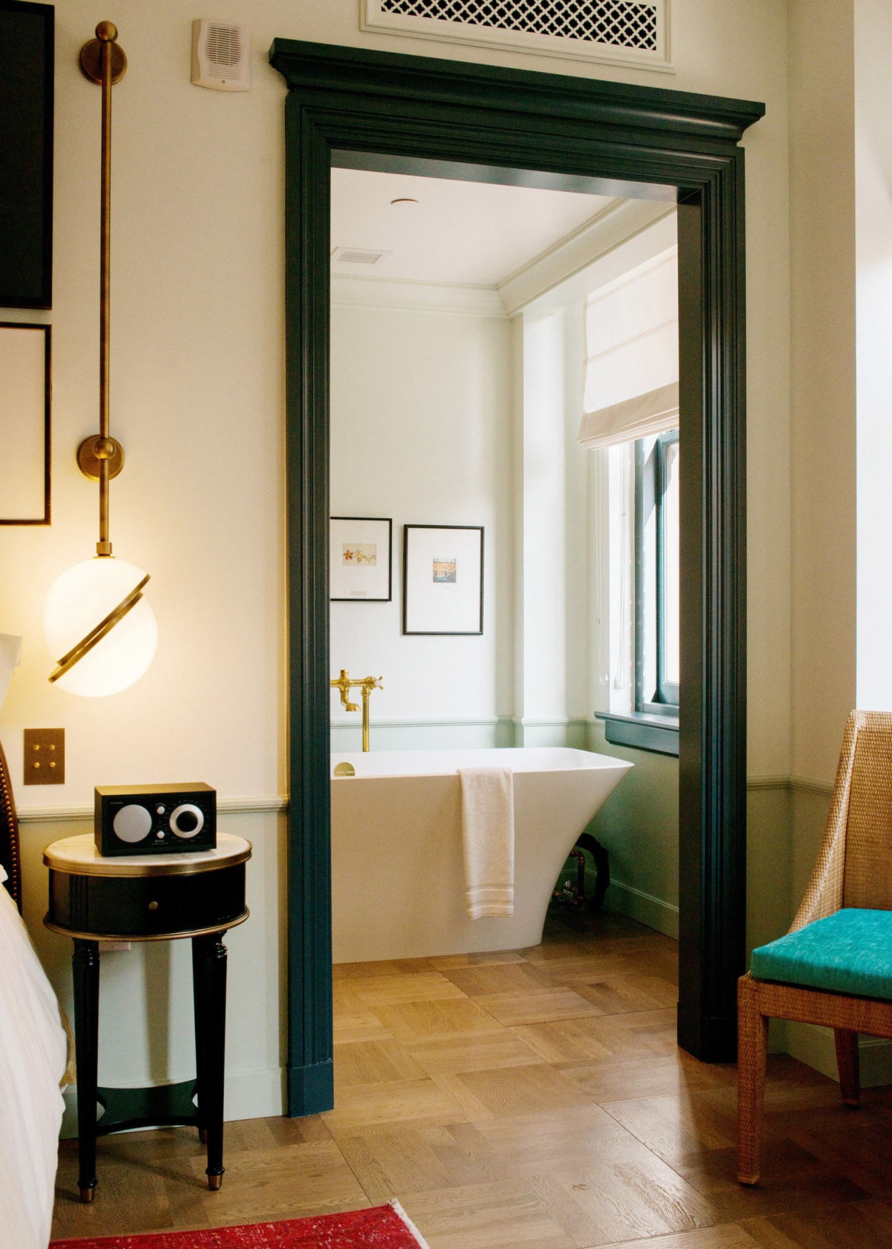 NoMad Los Angeles guest room bathroom with green-framed doorway, white soaking tub, brass fixtures and modern furnishings.