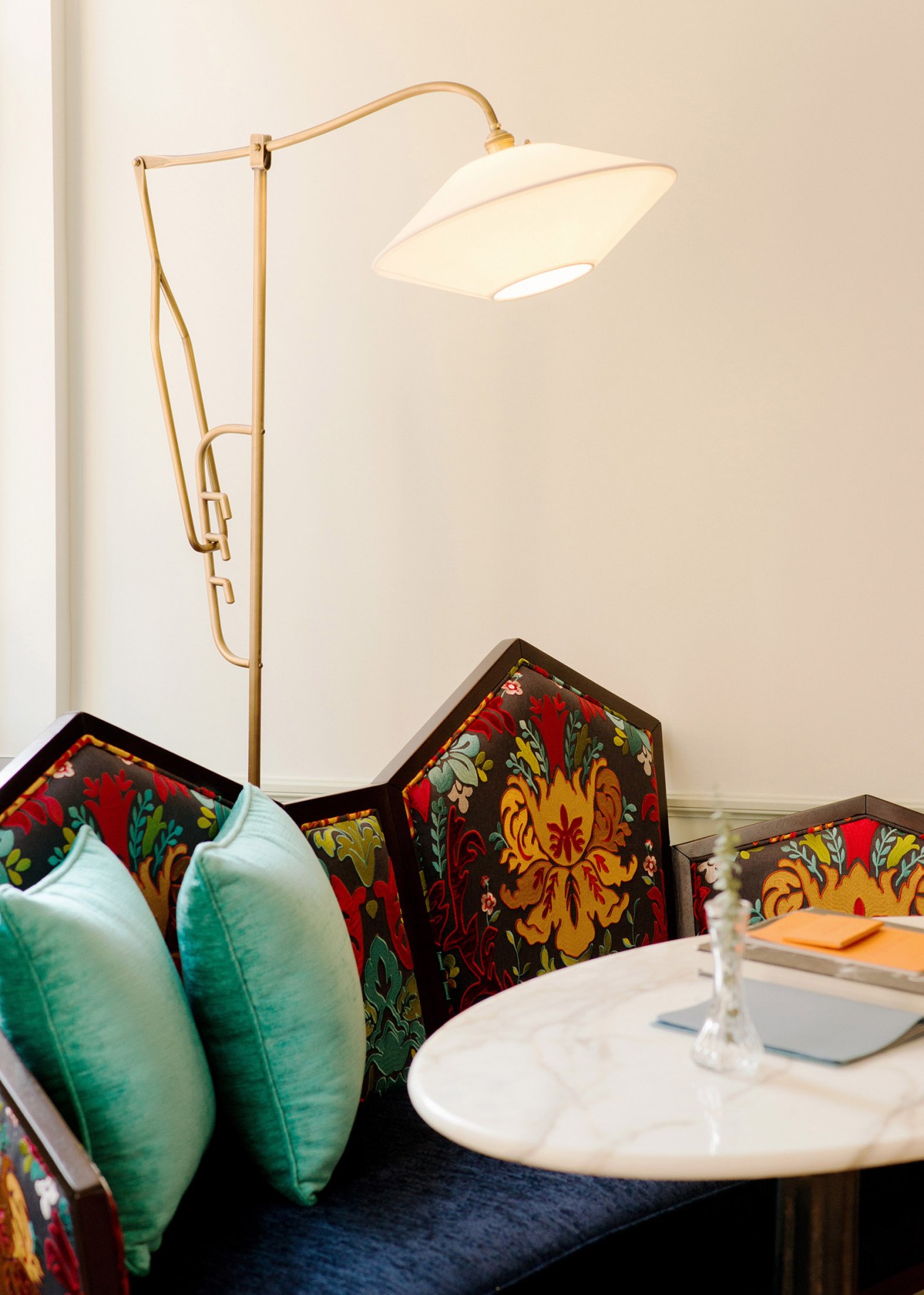 Hotel interior detail showing ornate patterned chair upholstery with brass floor lamp and white table setting.
