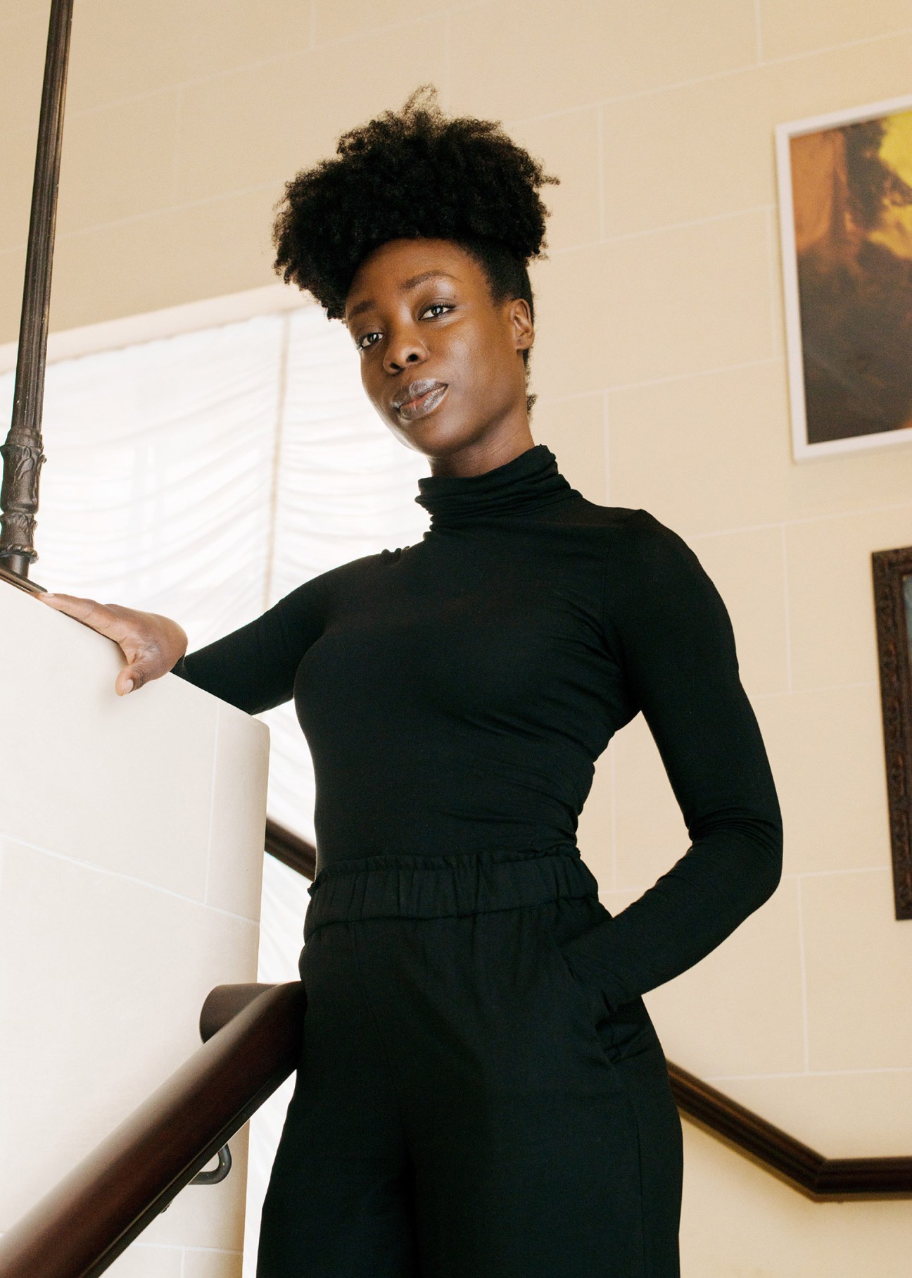 Hotel employee in black turtleneck posing by staircase in NoMad Los Angeles lobby.