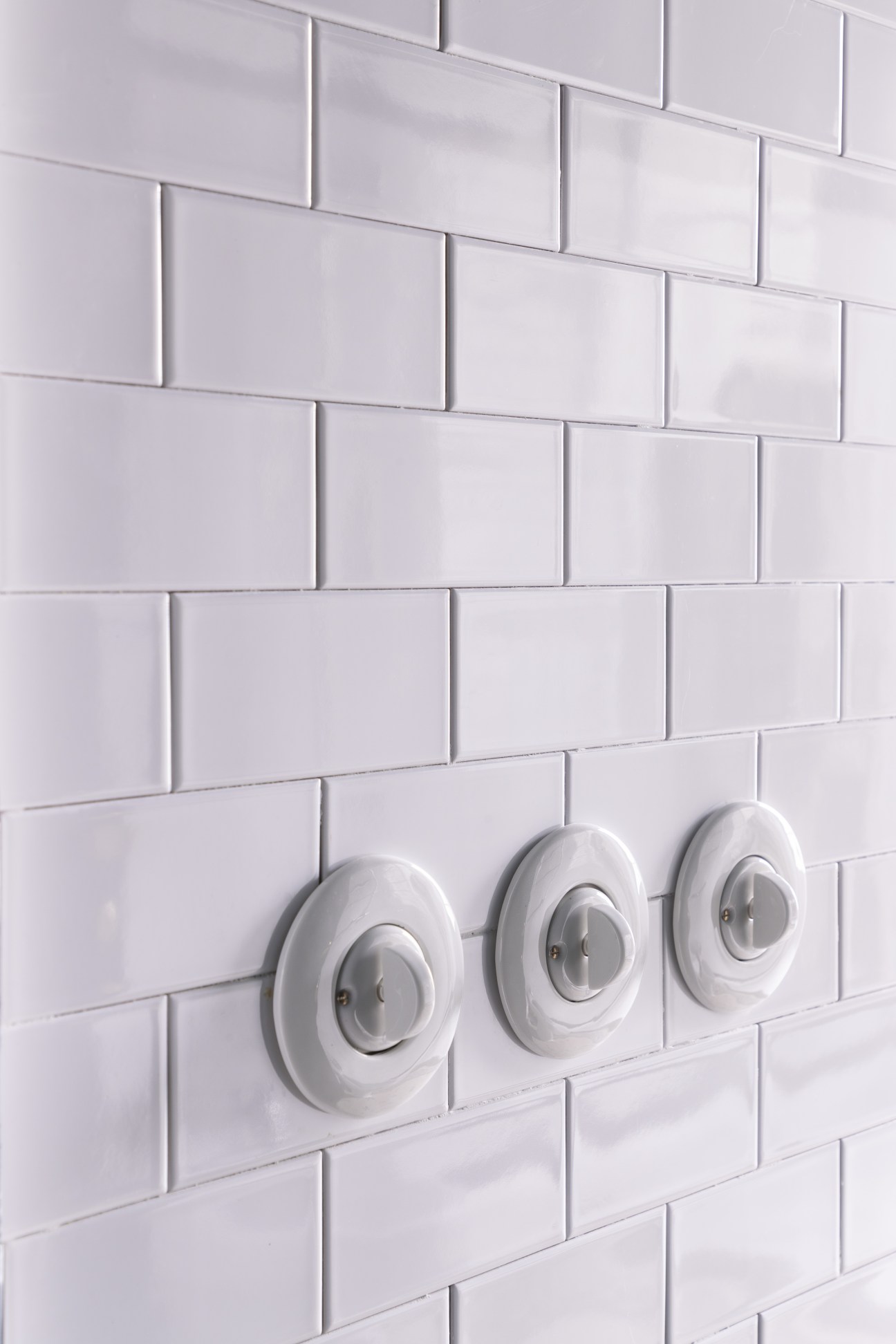 Three custom porcelain light switches mounted on white subway tile wall at Sister Hotel Milan.