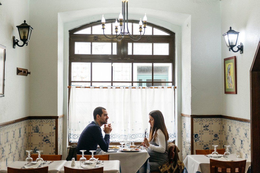 A man and woman dining at a table in a traditional Portuguese restaurant with tiled walls and lantern lighting