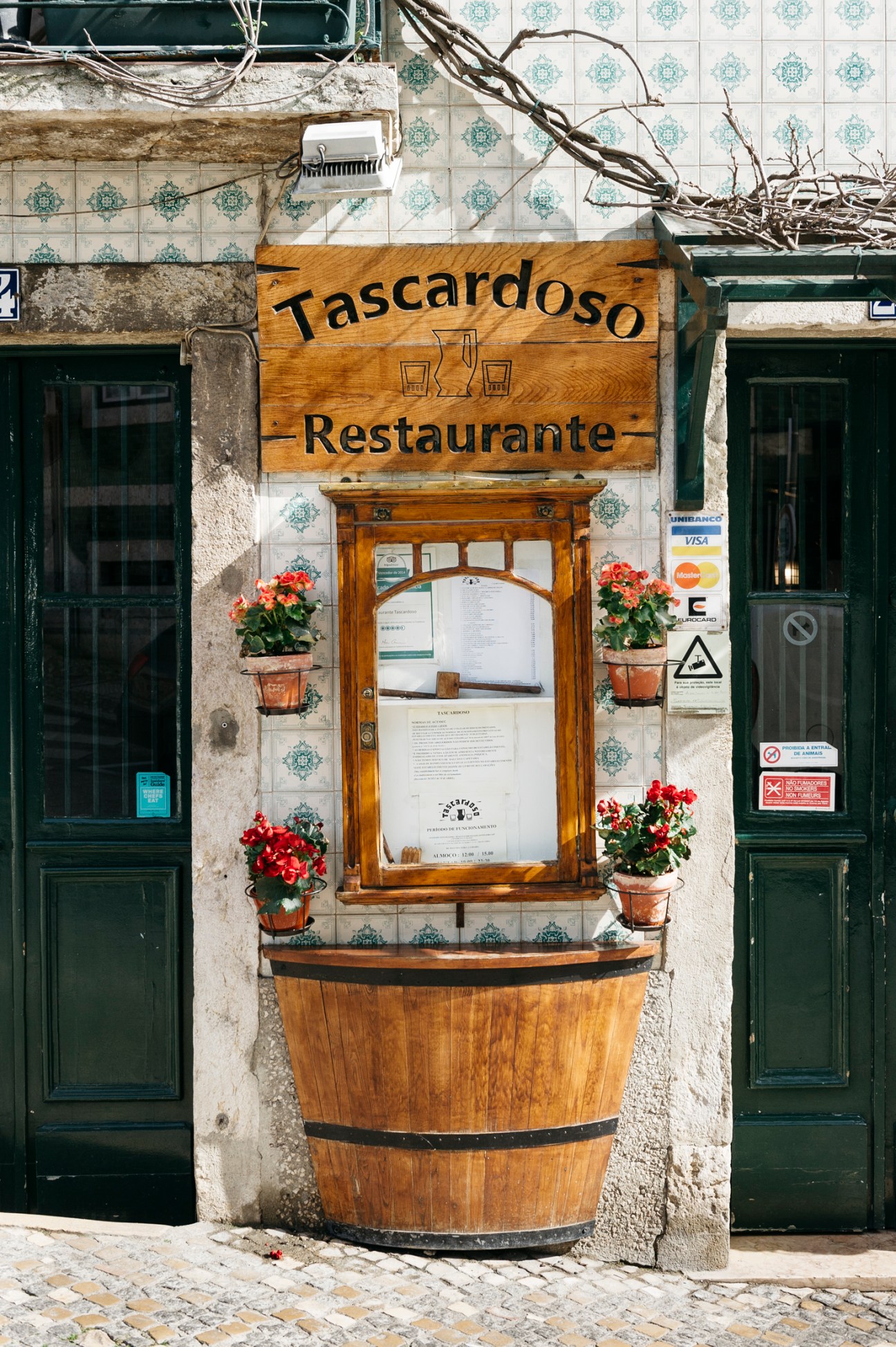 Wooden sign reading Tascardoso Restaurante with menu board below and potted flowers on tiled building facade
