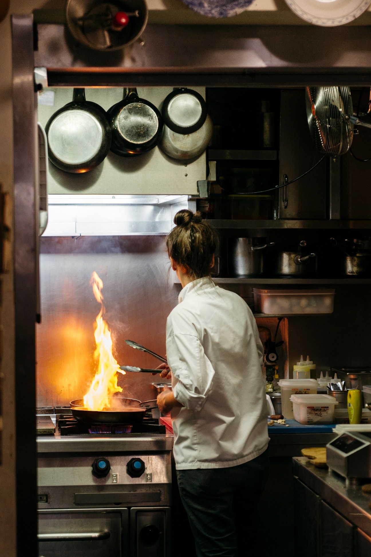 Chef in white coat cooking with flames rising from pan in professional kitchen