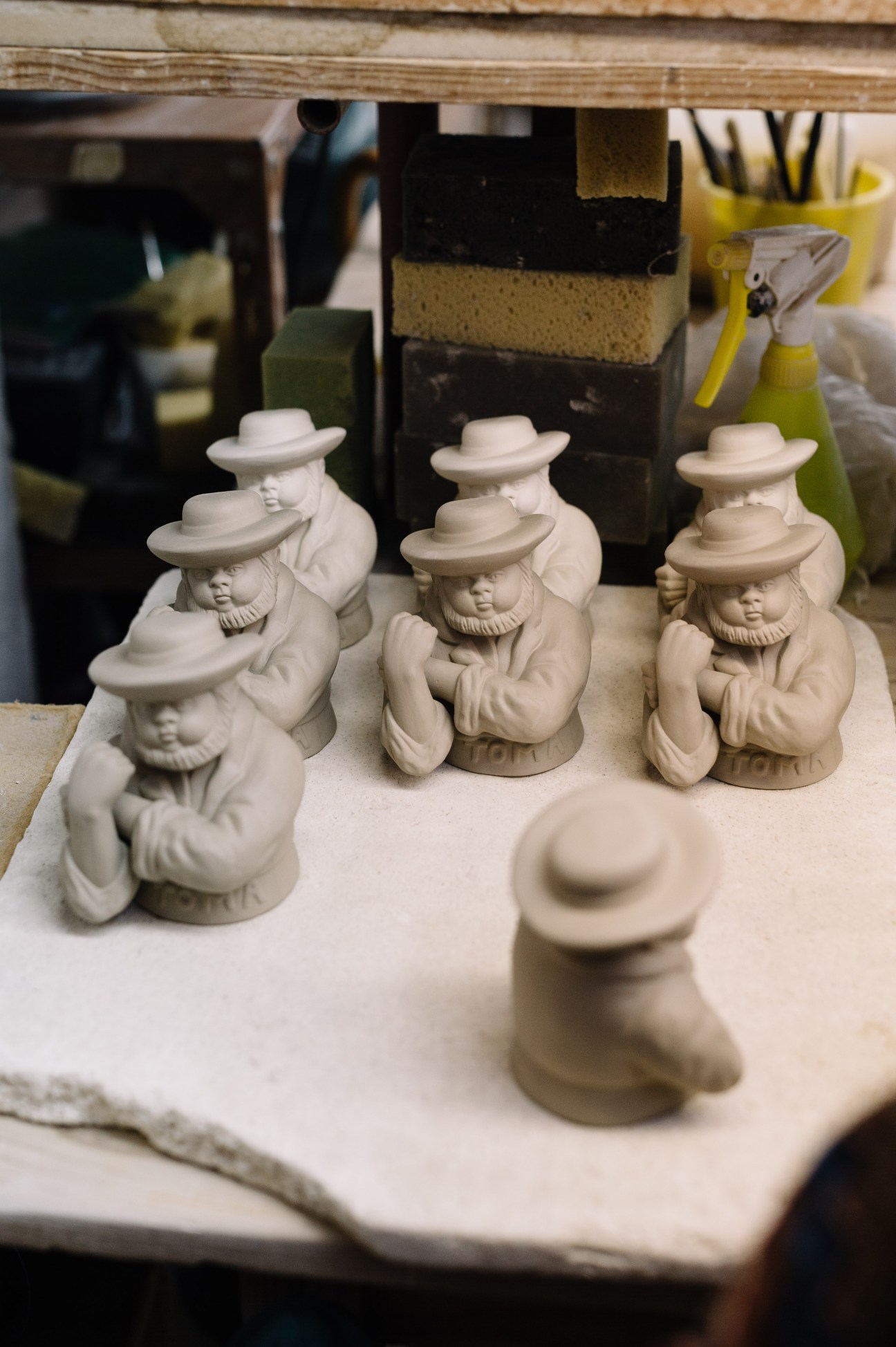 Unfired ceramic figurine pieces wearing hats arranged on a work surface in the Bordallo Pinheiro factory.