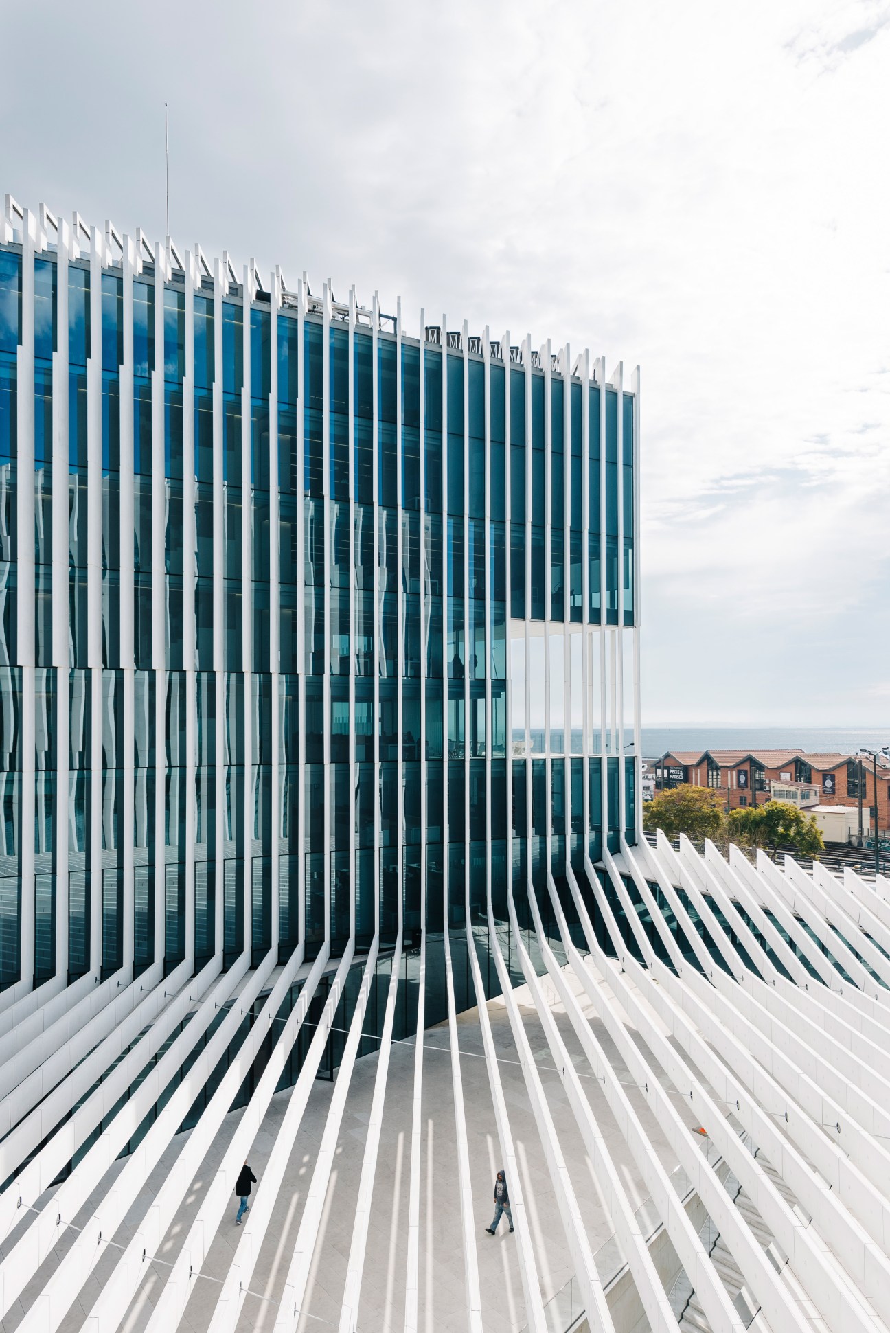Modern office building exterior with white concrete vertical louvers providing shade, overlooking waterfront buildings.