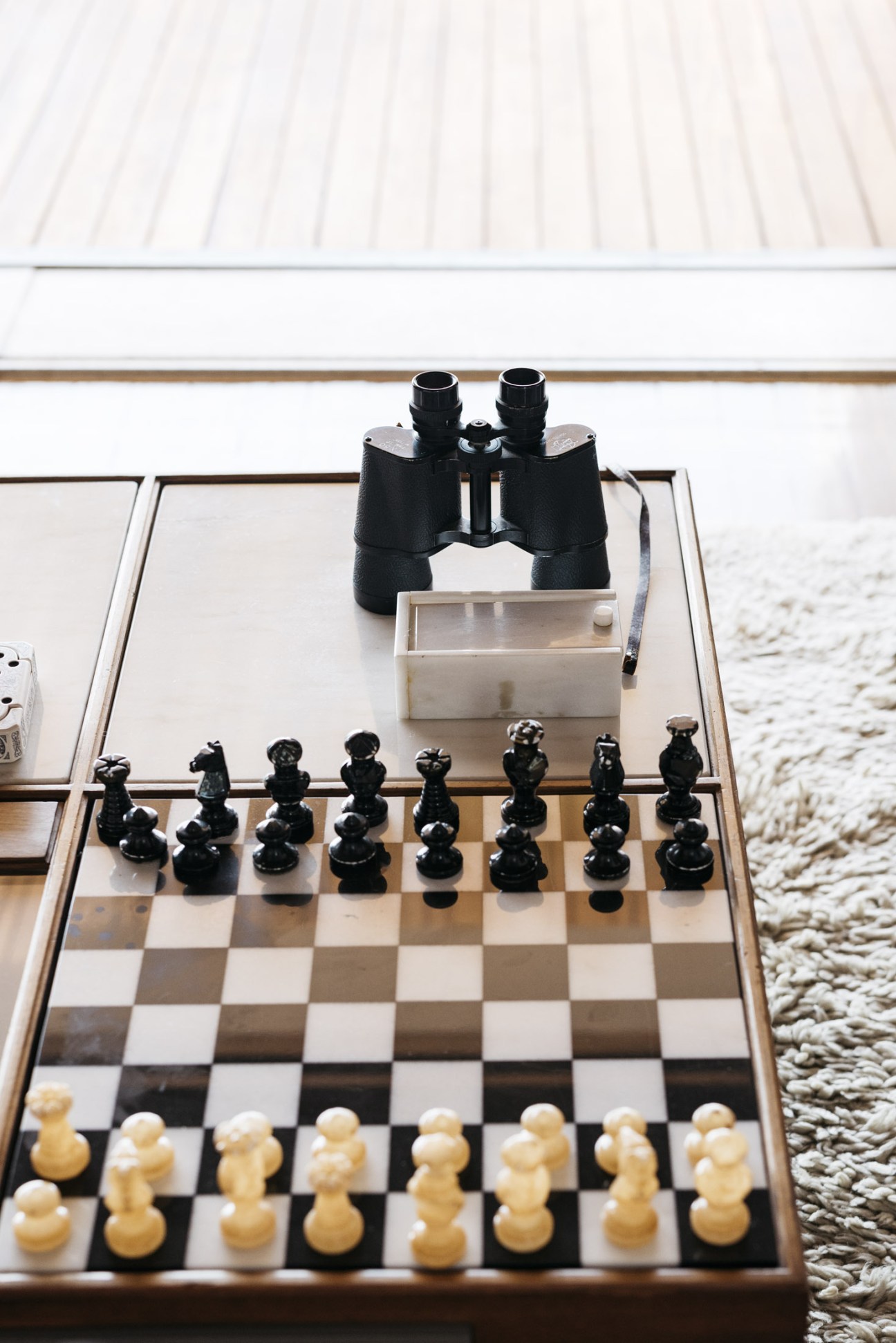 A chessboard with black and white pieces set up for play, featuring a built-in stereo system and binoculars on top, overlooking a coastal view.