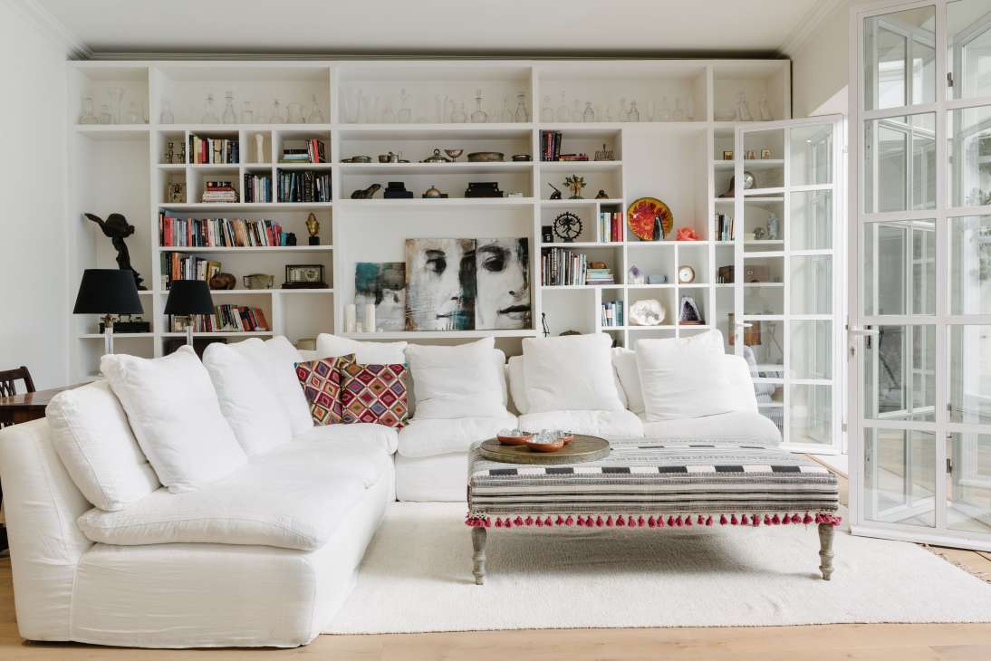 A modern white living room with floor-to-ceiling shelving, white sectional sofa, and abstract artwork at Casa Fuzetta.