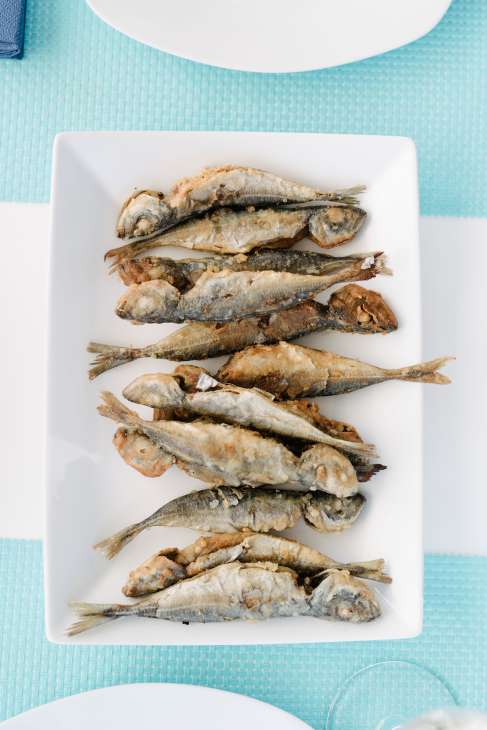 Plate of whole grilled small fish arranged in rows on white rectangular platter on turquoise textured surface