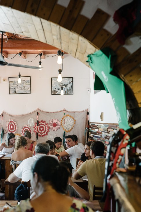 Interior of Bioco restaurant with diners seated at wooden tables beneath hanging pendant lights and decorative textile wall hangings.