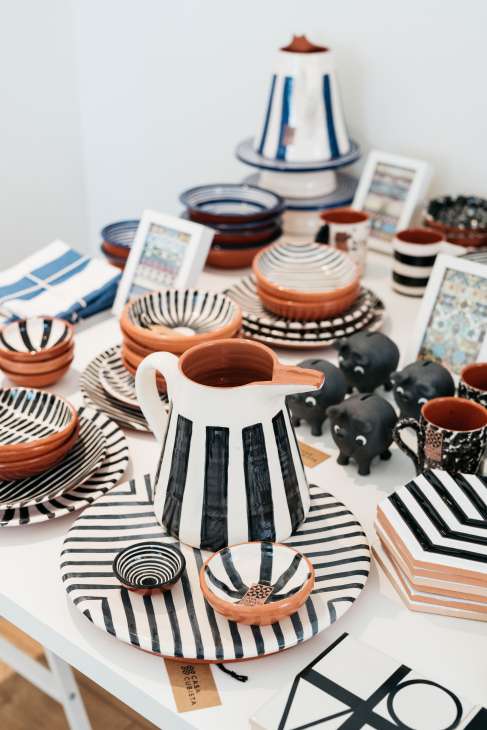 Casa Cubista ceramic tableware collection displayed on a white surface, featuring striped plates and bowls in terracotta, black, and white.
