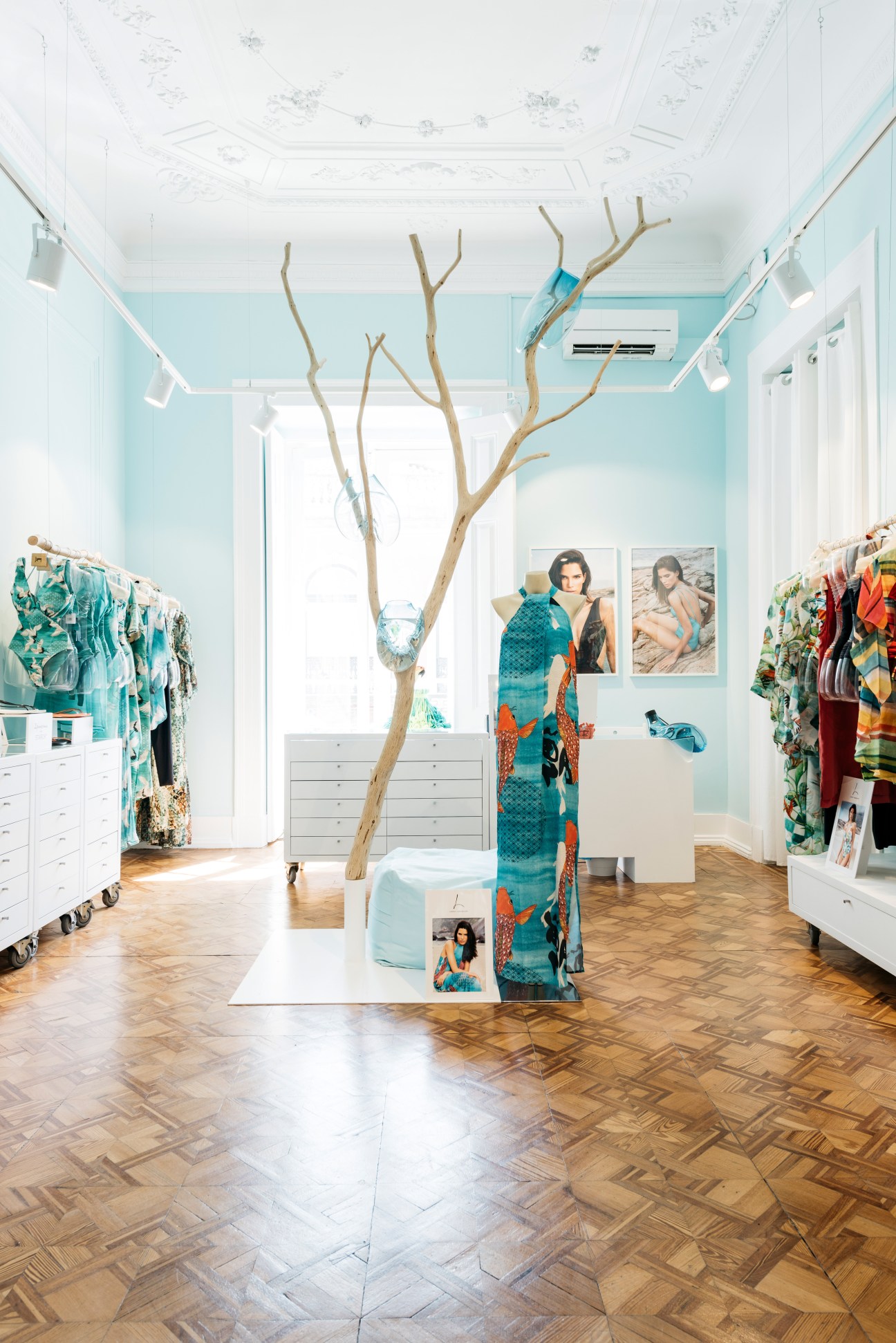 Interior of Lenny Niemeyer shop with colorful swimwear displayed on racks, a sculptural branch installation, and turquoise walls.