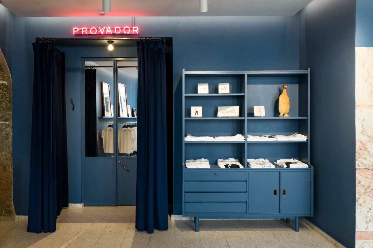 Interior of Lapo shop in Lisbon with navy walls, blue cabinetry, neon Provador sign, and dressing room curtains.