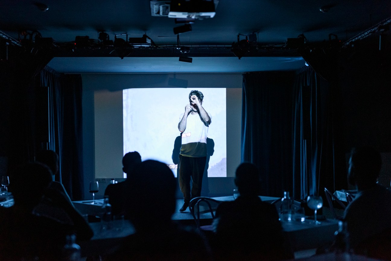 A comedian performs on stage at Lapo in Lisbon, with audience members silhouetted in the foreground.