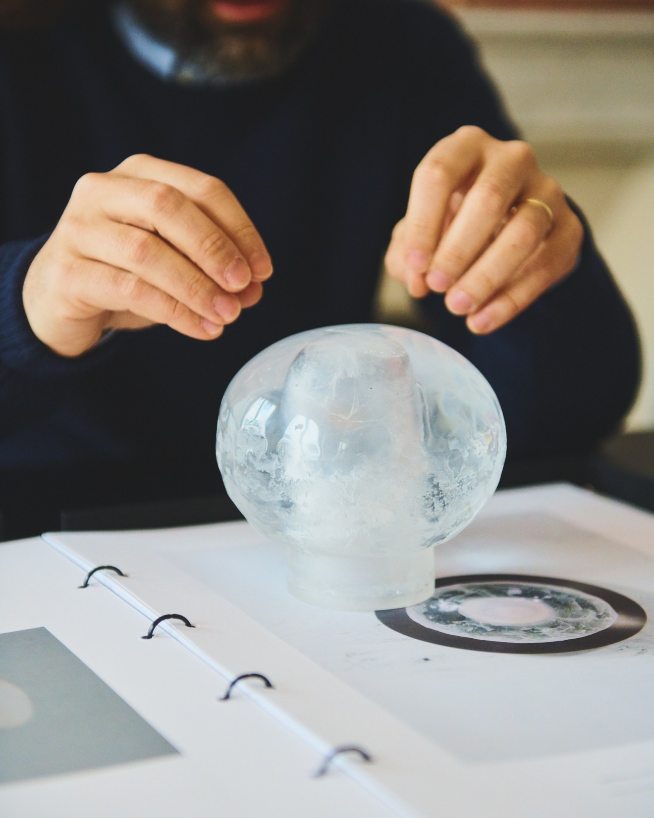 Hands holding a translucent spherical glass object made through lost wax casting technique.