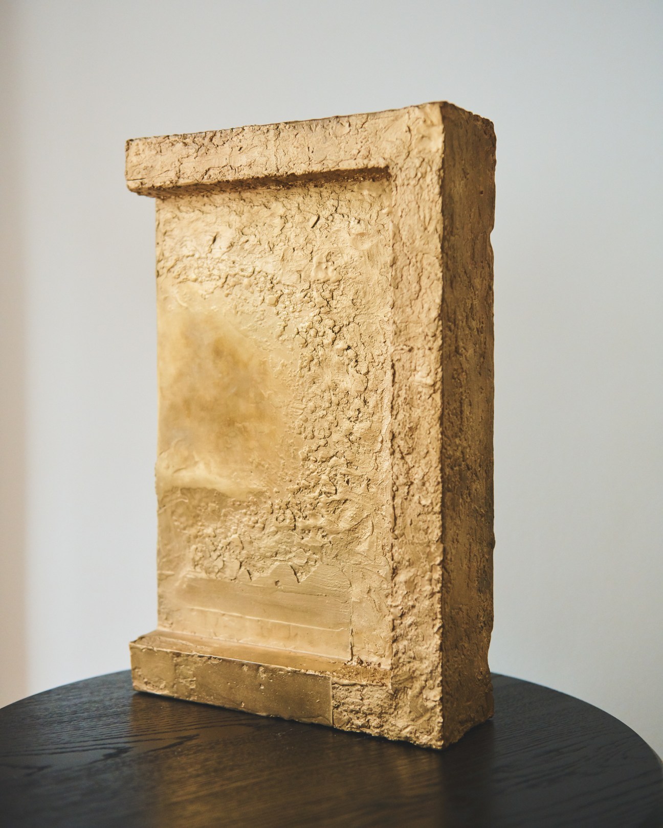 Minimalist bronze sculptural object with textured surface on dark wooden table.