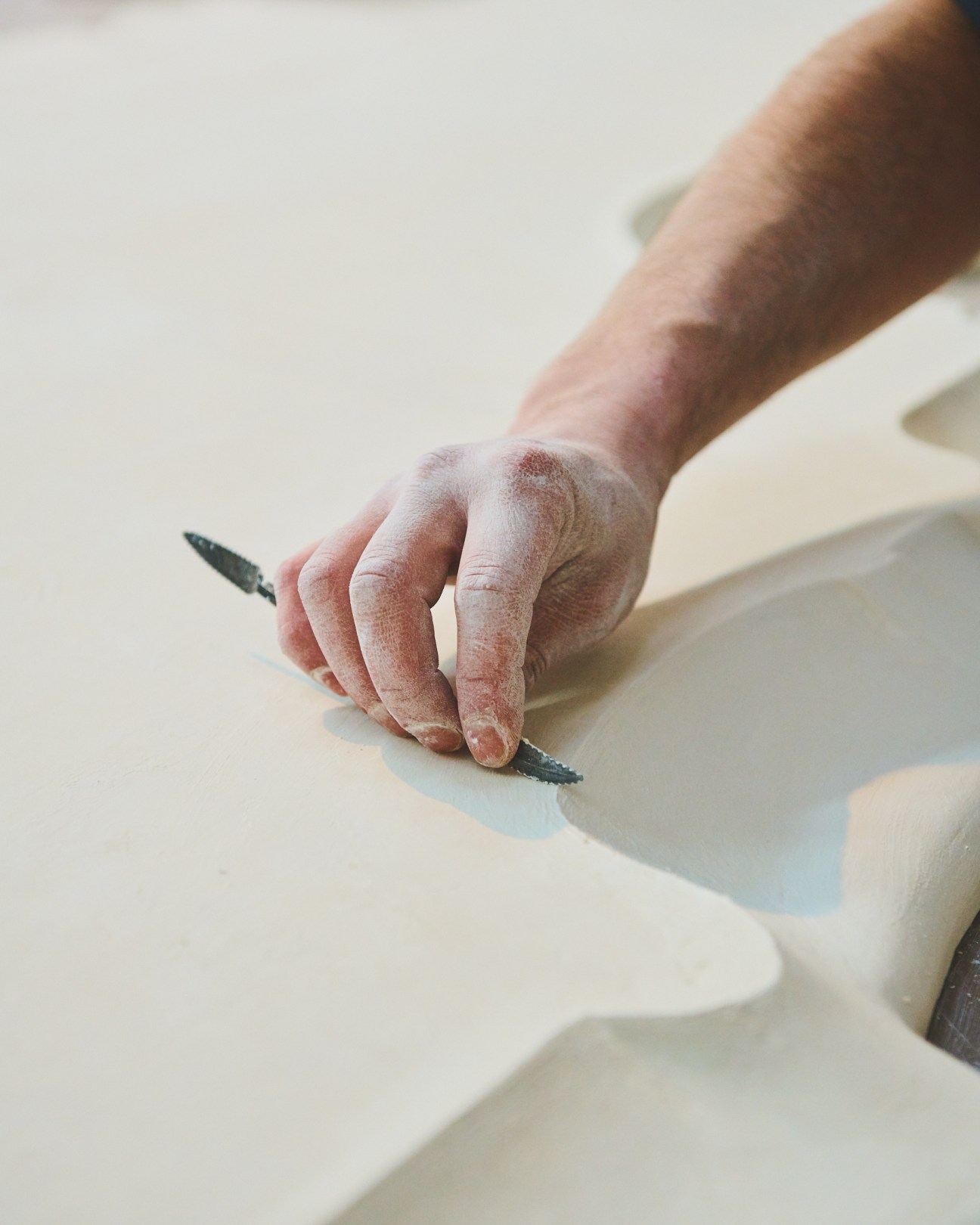 Craftsperson's hand working plaster with a tool, demonstrating traditional handworking technique.