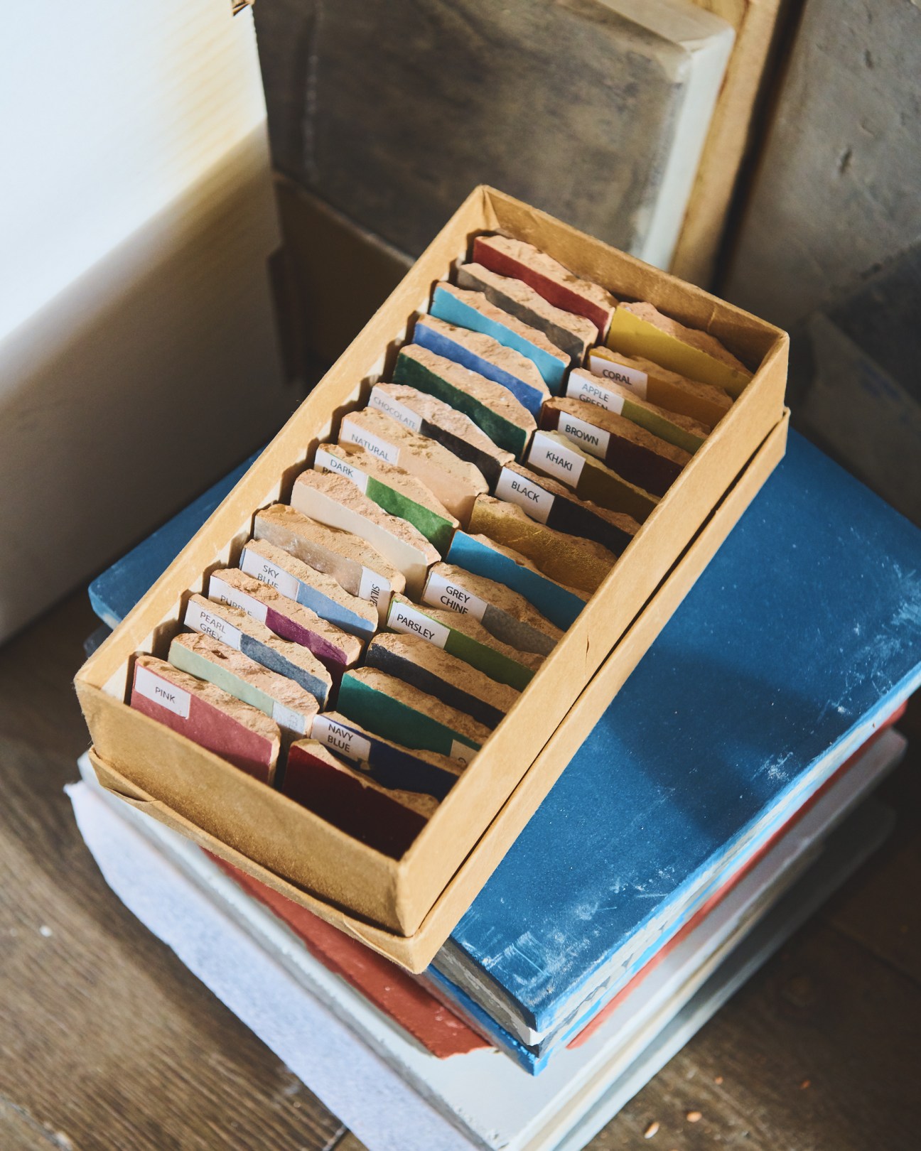 Wooden box containing organized fabric and material samples with labels in various colors including blue, green, burgundy and natural tones.