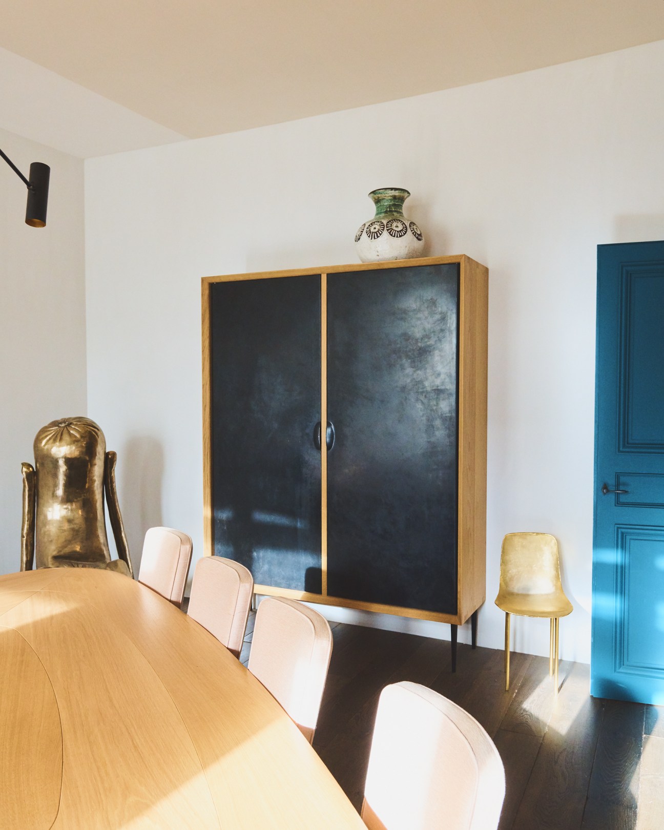 Meeting room with wooden table, pink chairs, wooden cabinet with black doors, and blue door at Pierre Yovanovitch's studio.