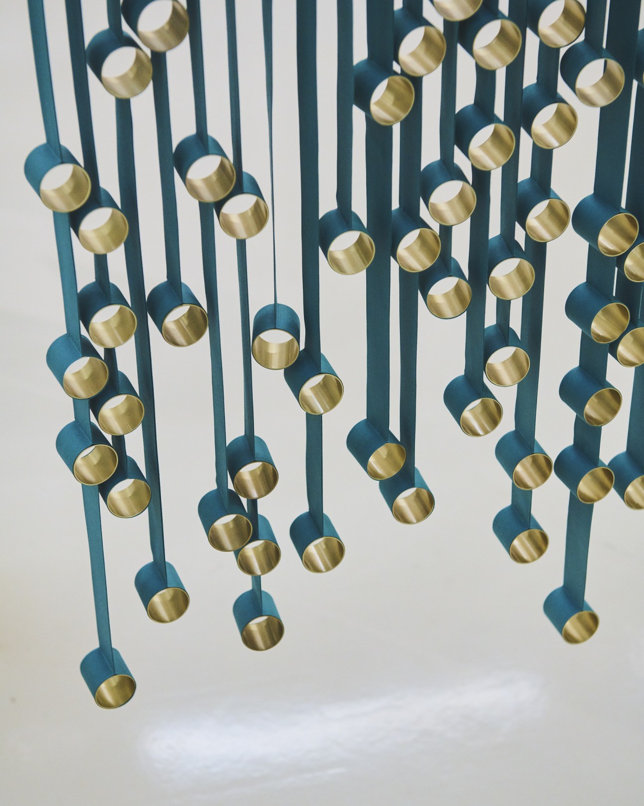 Hanging mobile with teal rods and brass spheres suspended against white background, Studio MTX designs.