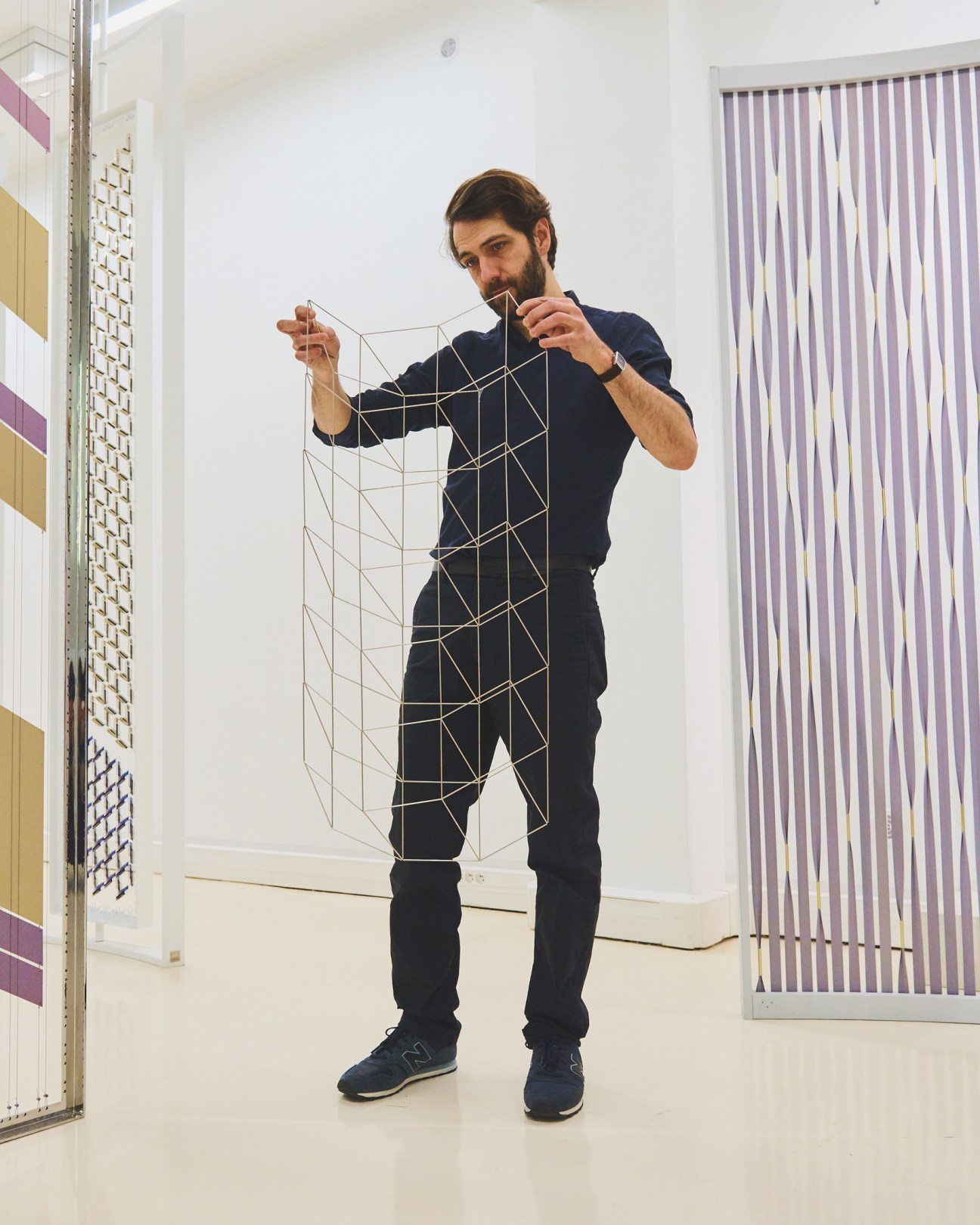 Mathieu Bassée of Studio MTX holds up a geometric wire and gold-thread design sample in a bright studio space.