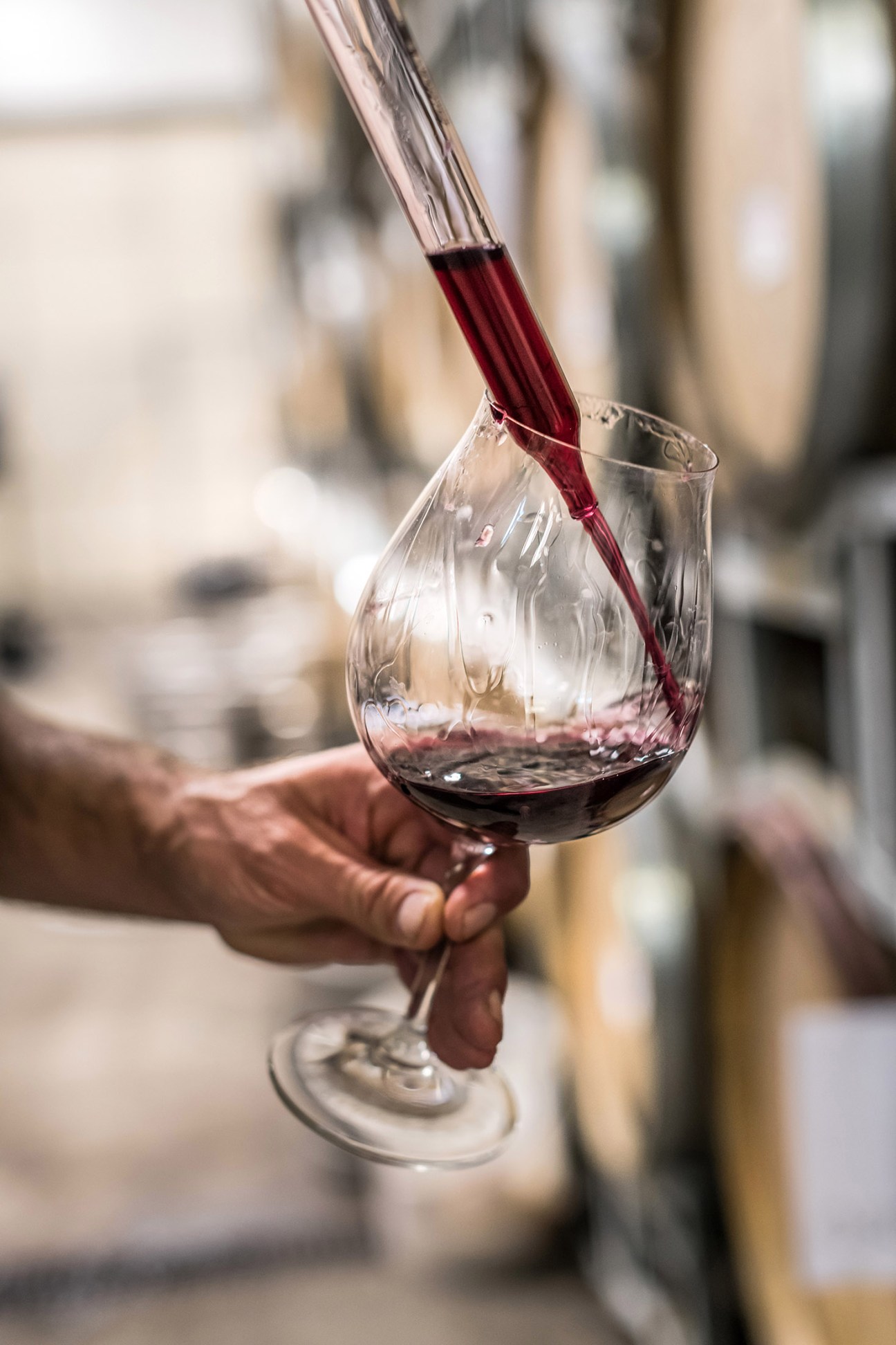 Red wine being poured from a bottle into a clear glass held in someone's hand.
