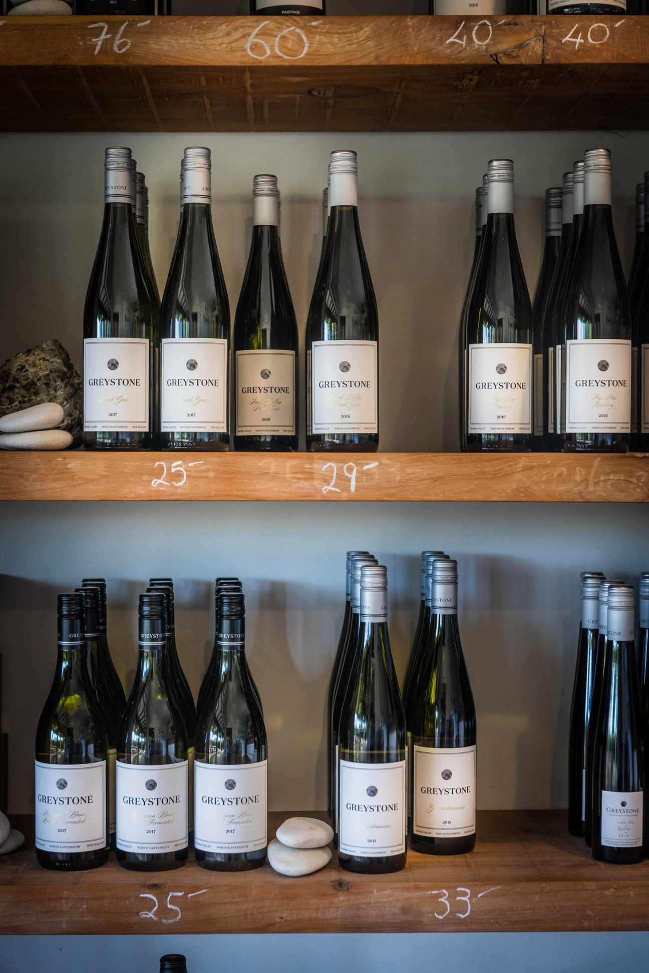 Greystone wine bottles displayed on wooden shelves with handwritten vintage numbers.