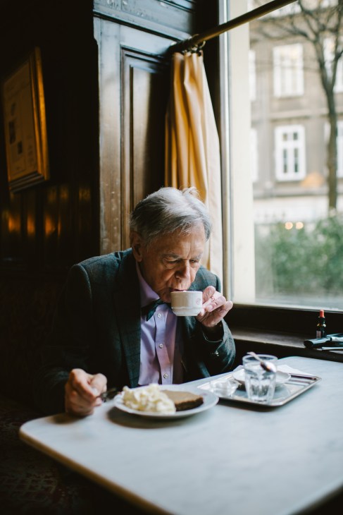 Older man in blazer drinking coffee by window at Café Sperl, Vienna.