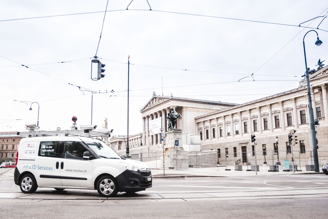 White iNovitas mobile-mapping van with roof cameras on Vienna street near parliament building.