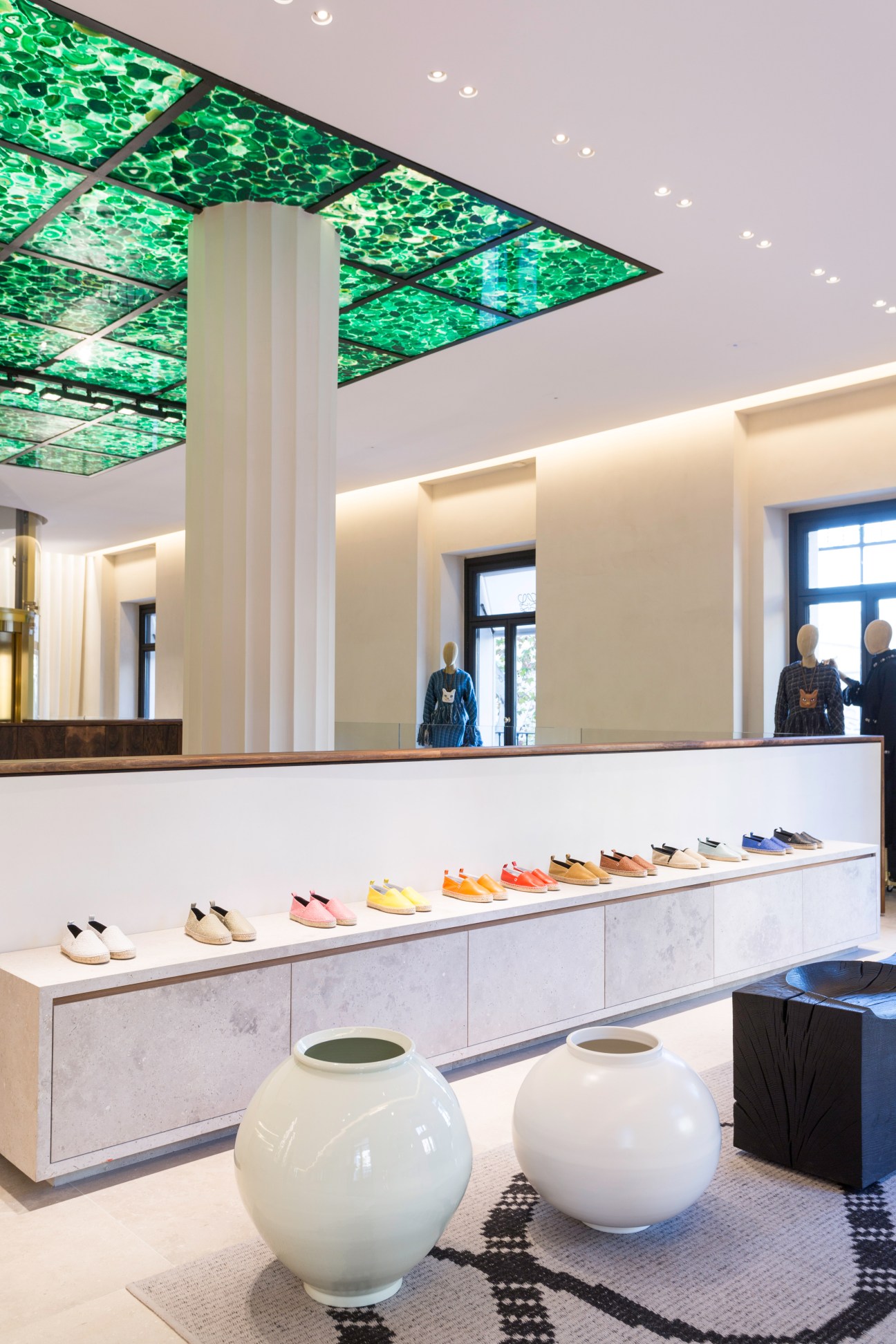 Interior of Casa Loewe flagship store showing colorful espadrilles displayed on a long counter with green ceiling panels above.